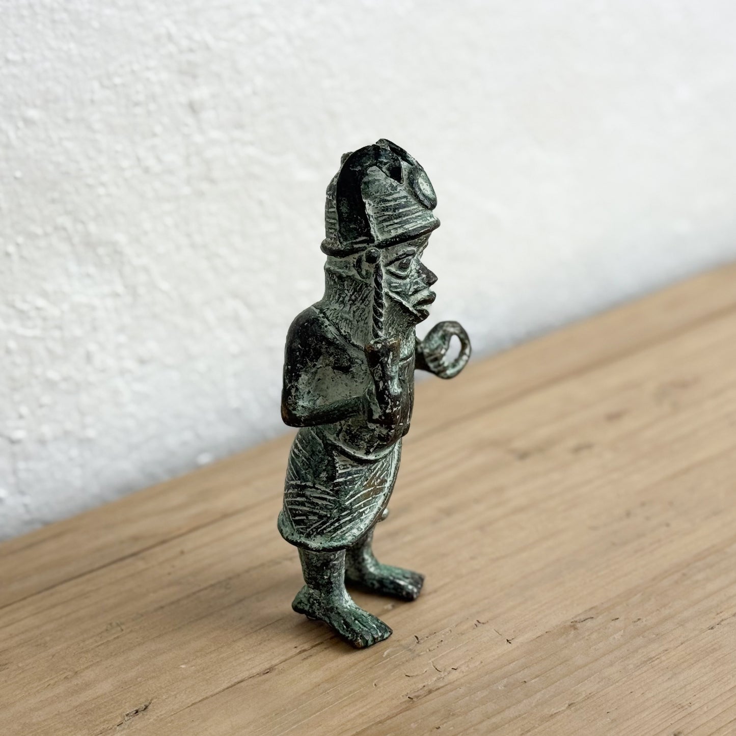 Bronze figurine of a warrior on a wooden surface with a white wall background