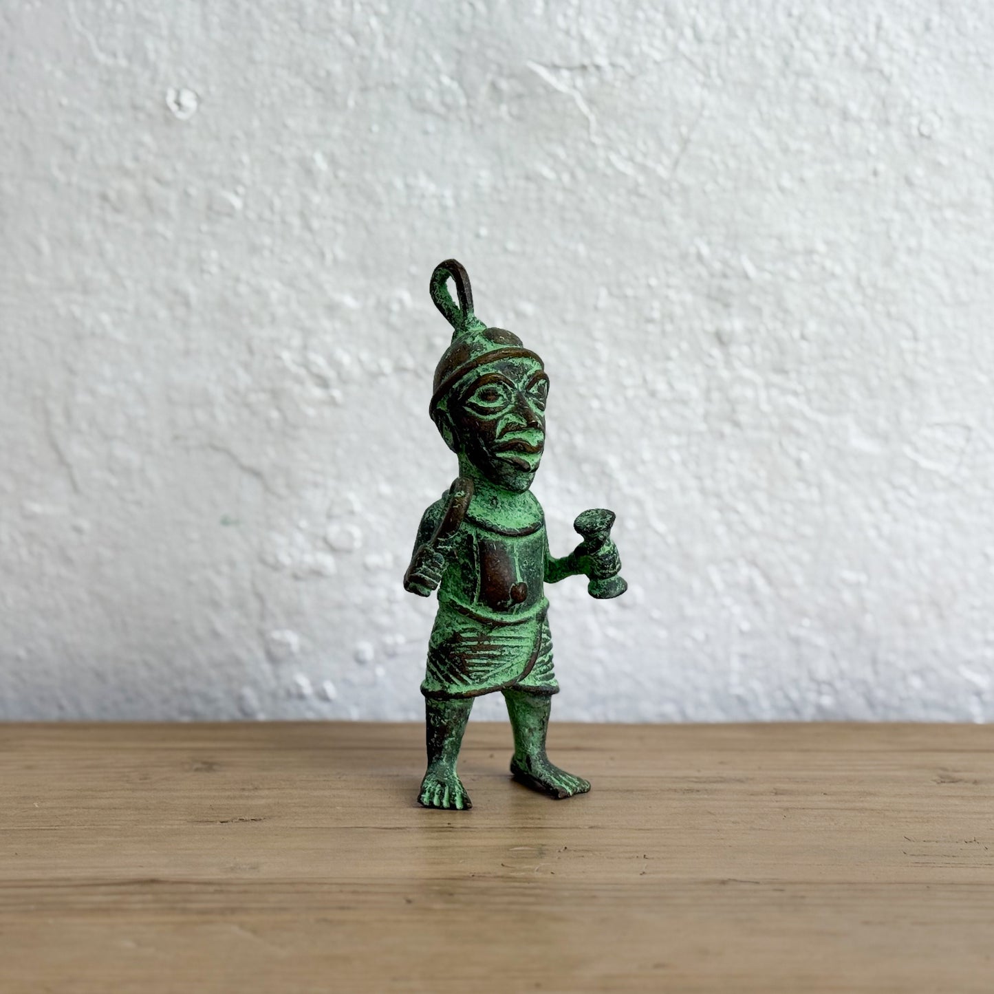 Bronze figurine with green patina on a wooden surface and white textured wall background