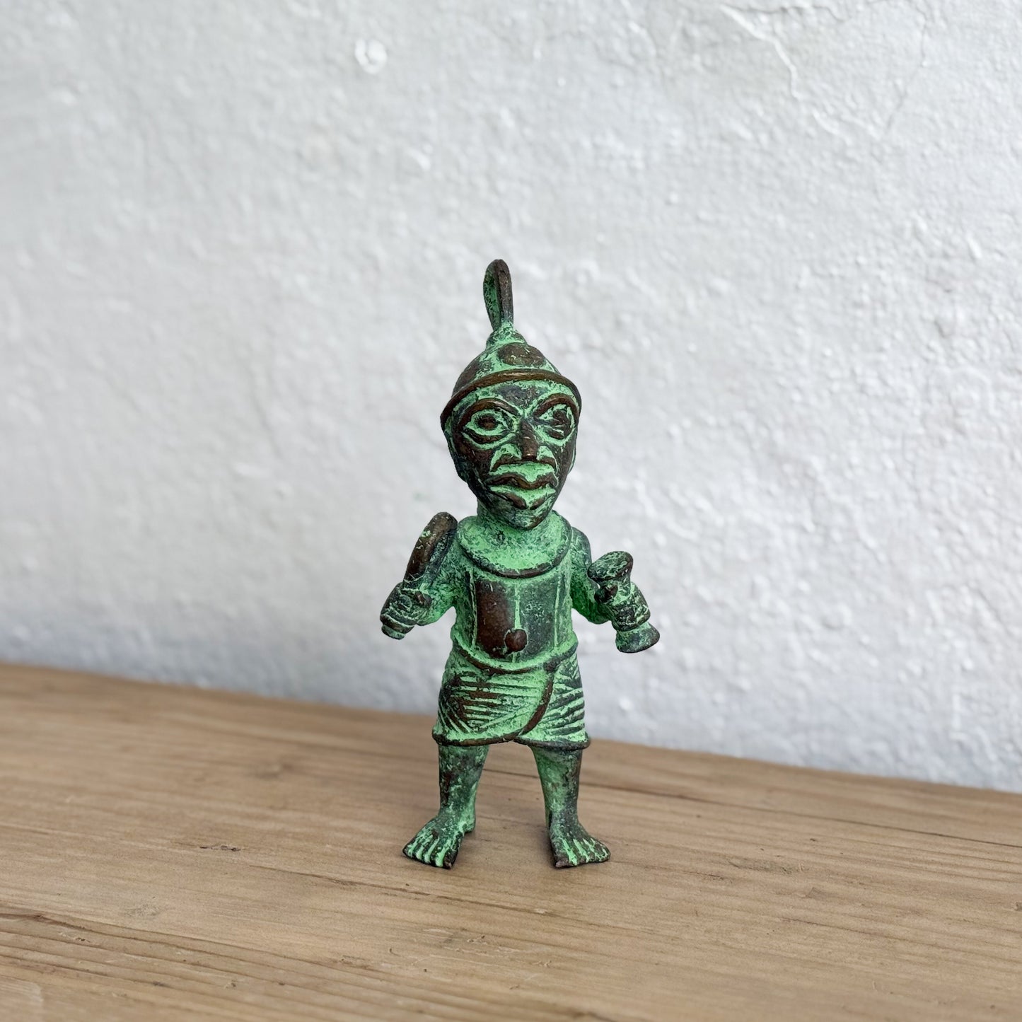 Green metallic figurine on a wooden surface with a white textured wall background