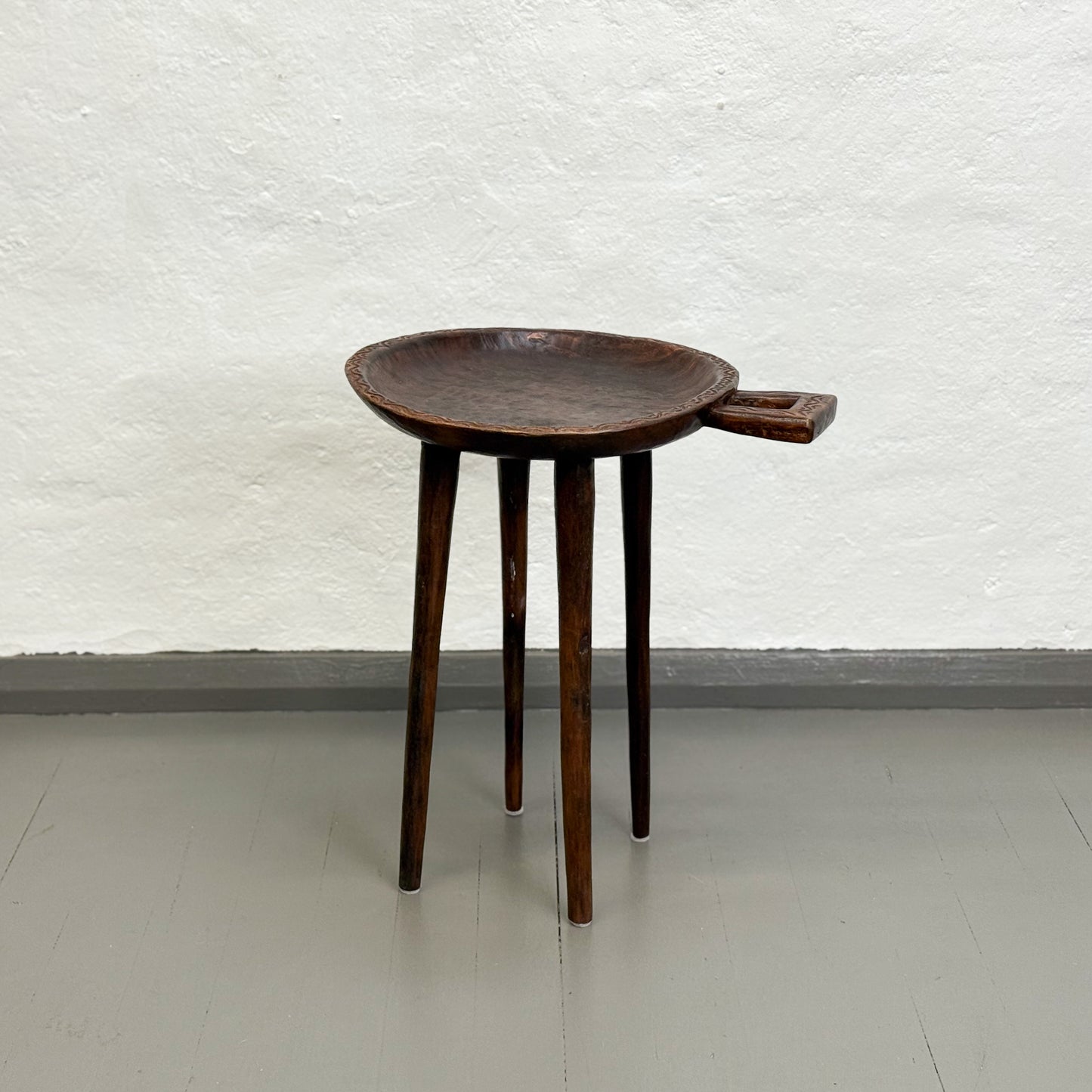Wooden side table with a tray on a white floor against a textured white wall
