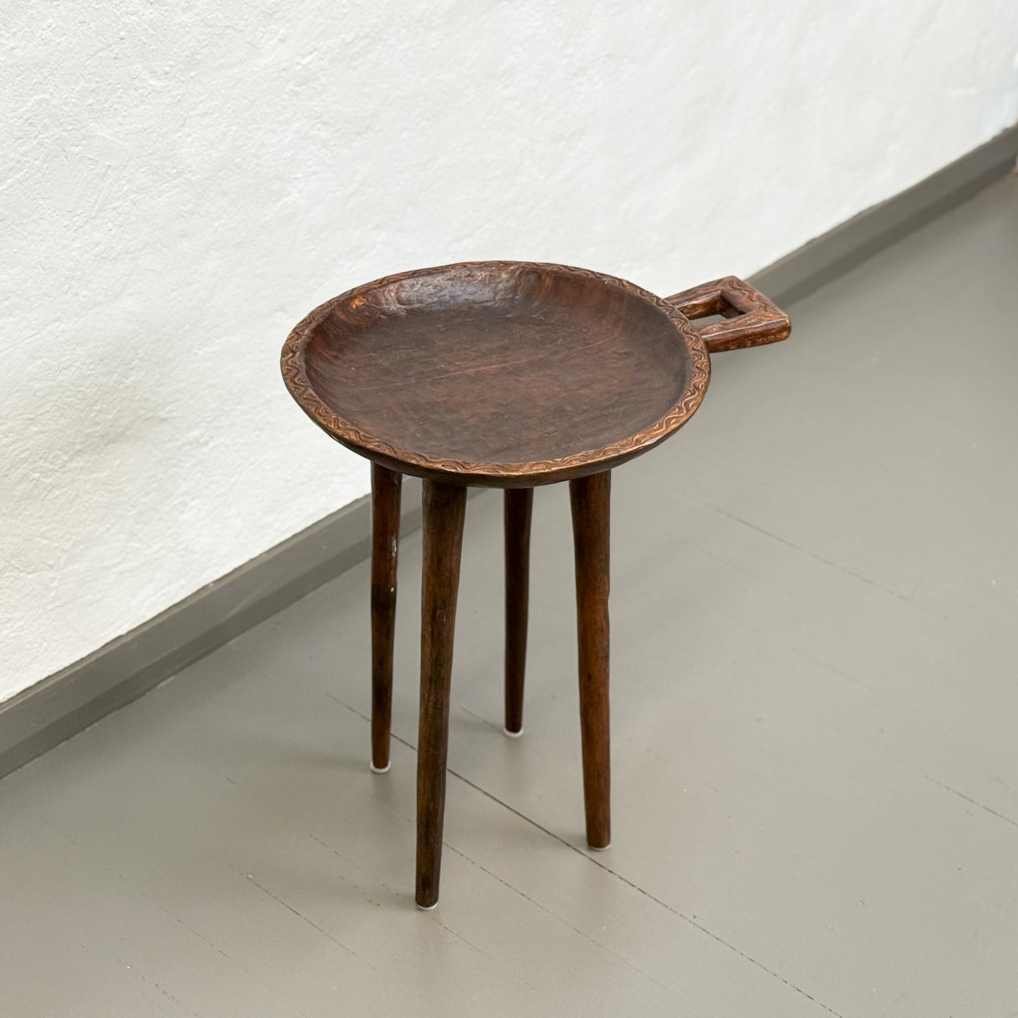 Small round metal table with a handle on a plain floor.