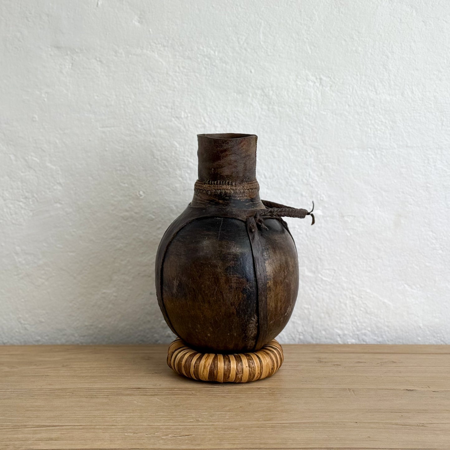Wooden vase with a textured surface on a wooden table against a white wall