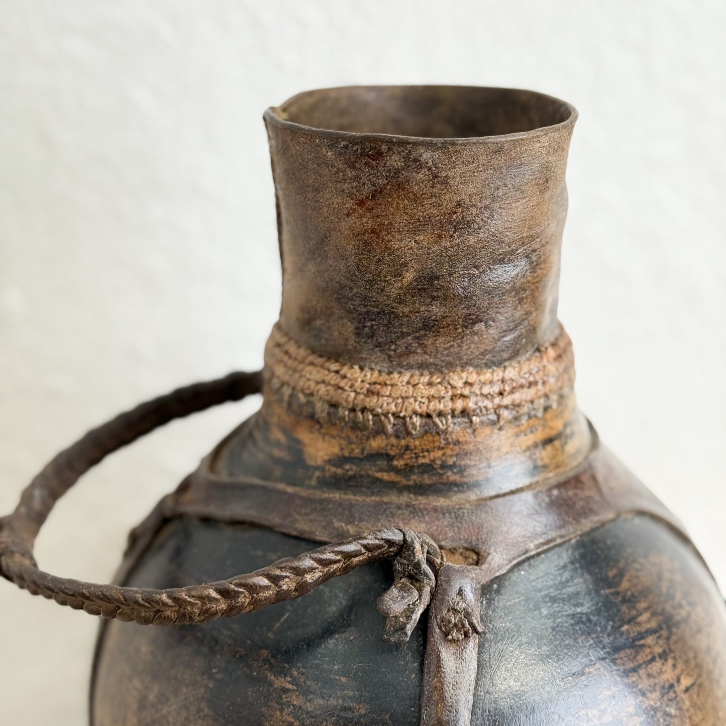 Close-up of an ancient bronze or copper pot with a rope handle on a light background