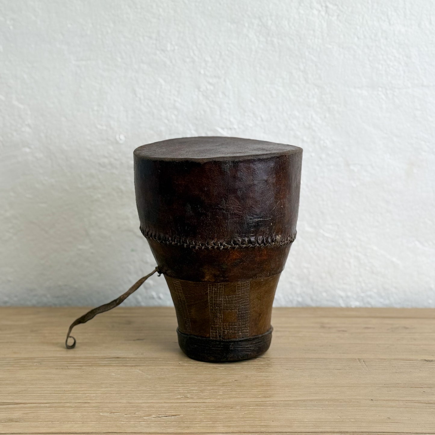 Wooden drum with leather rim on a wooden surface against a white wall