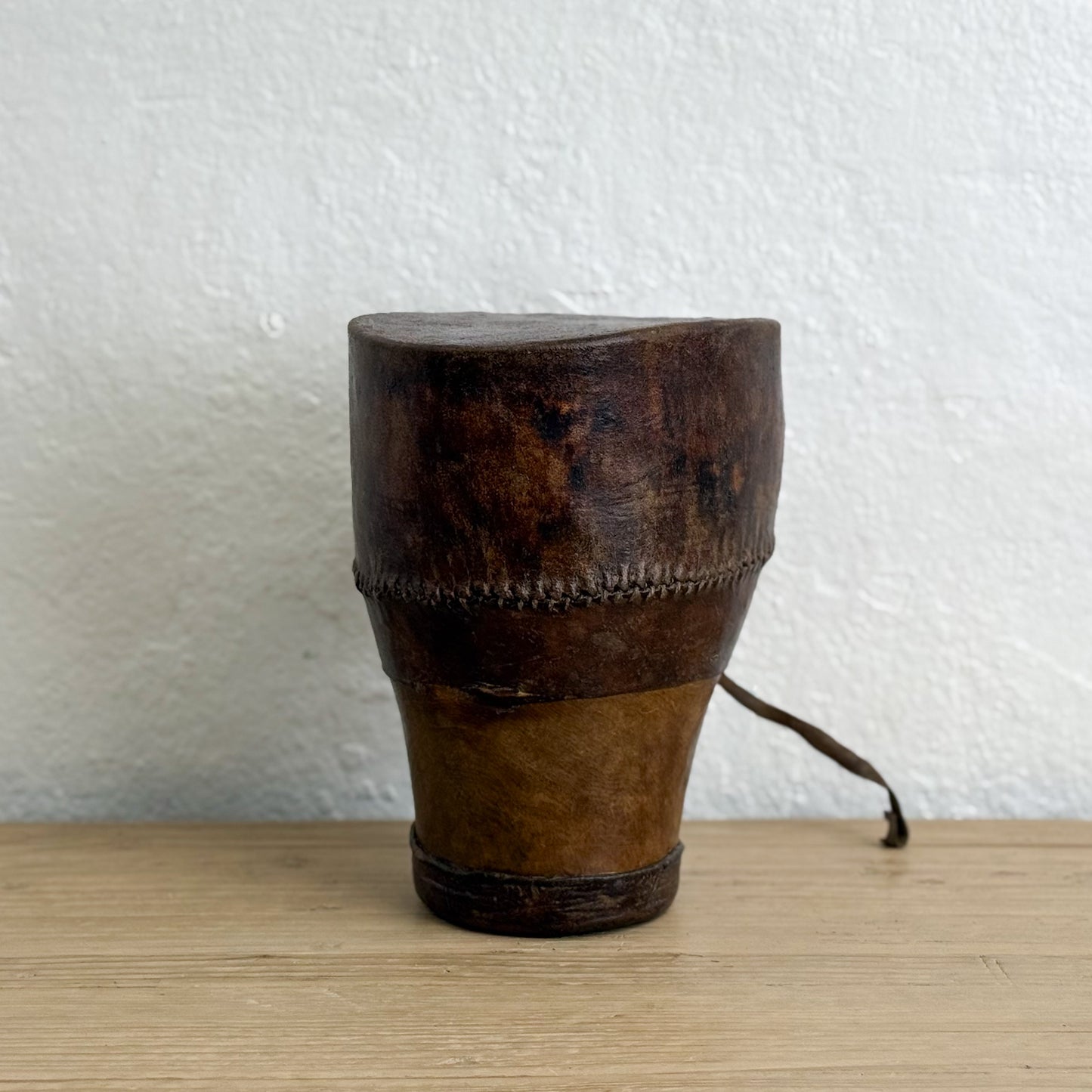 Wooden drum with leather skin on a wooden surface and white textured wall background