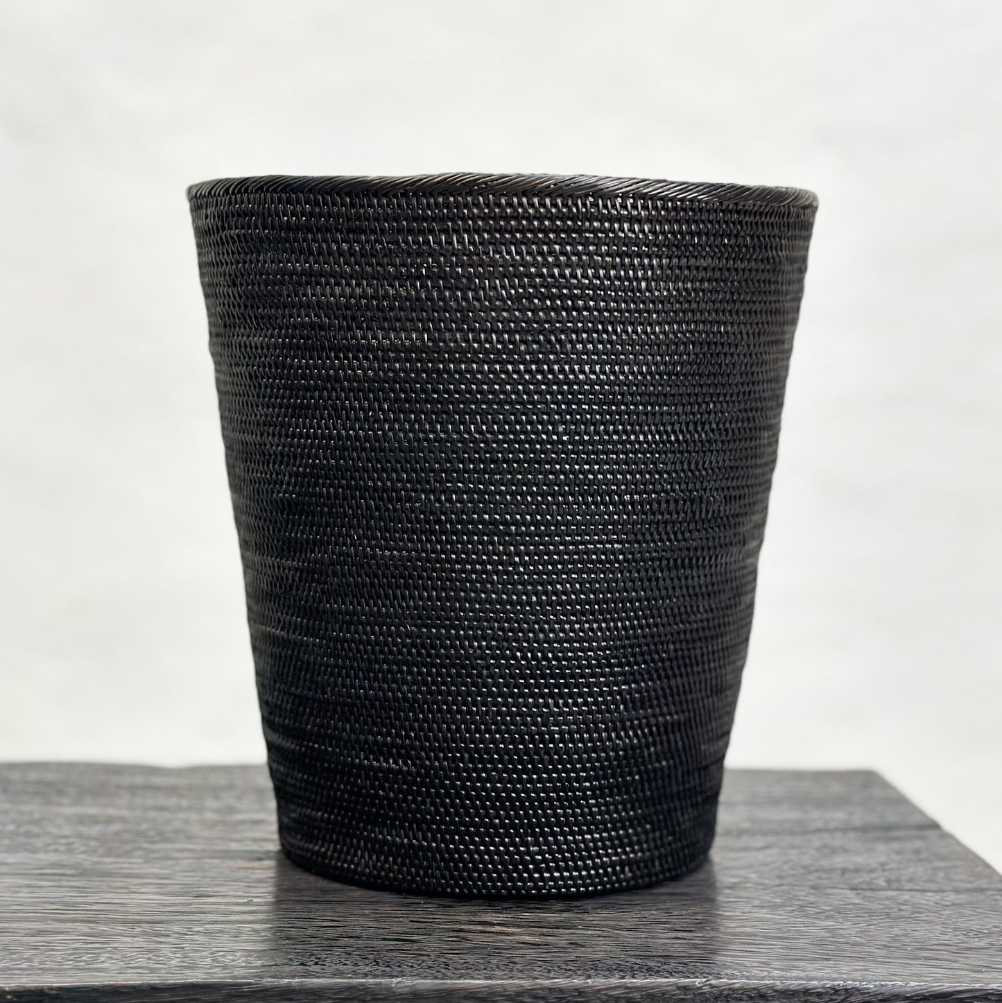 Two black tapered dustbins with a woven texture, placed on a dark surface.
