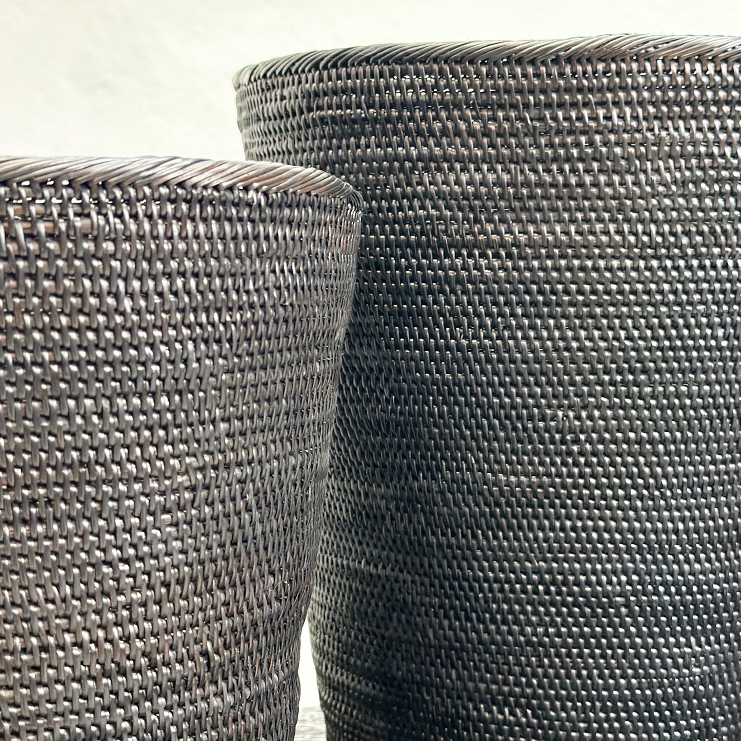 Two black tapered dustbins with a woven texture, placed on a dark surface.