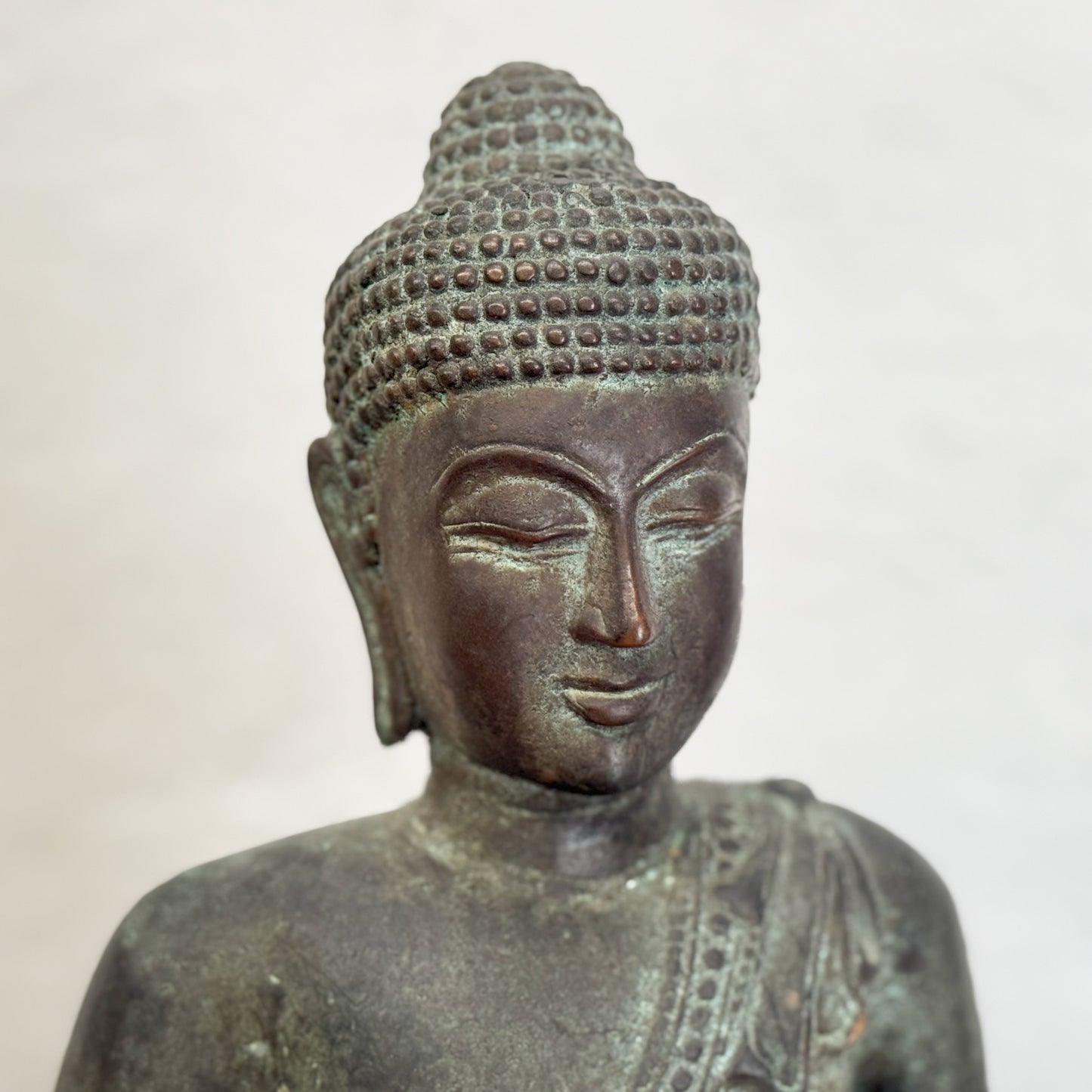 A bronze sculpture of a standing Buddha with hands outstretched, wearing a robe, placed on a black base.