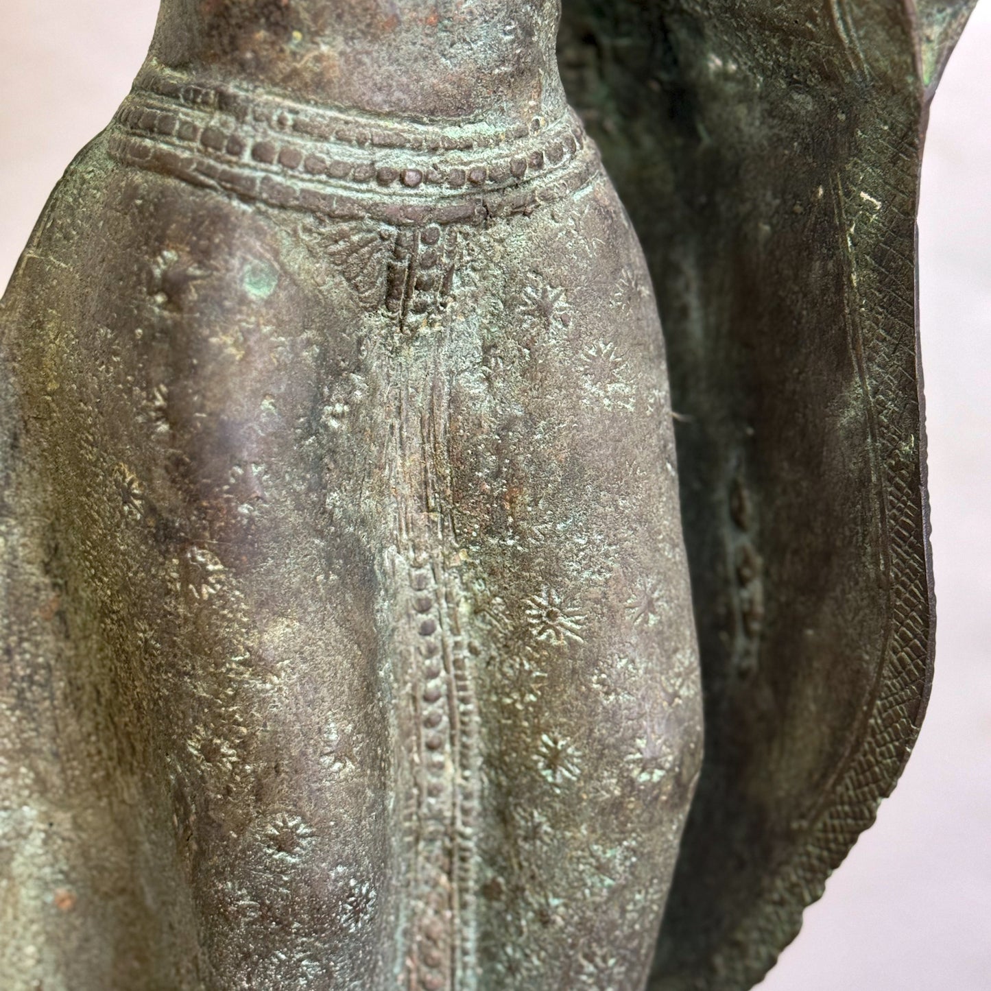A bronze sculpture of a standing Buddha with hands outstretched, wearing a robe, placed on a black base.