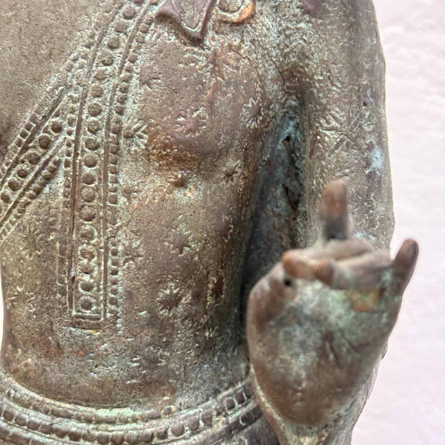 A bronze sculpture of a standing Buddha with hands outstretched, wearing a robe, placed on a black base.