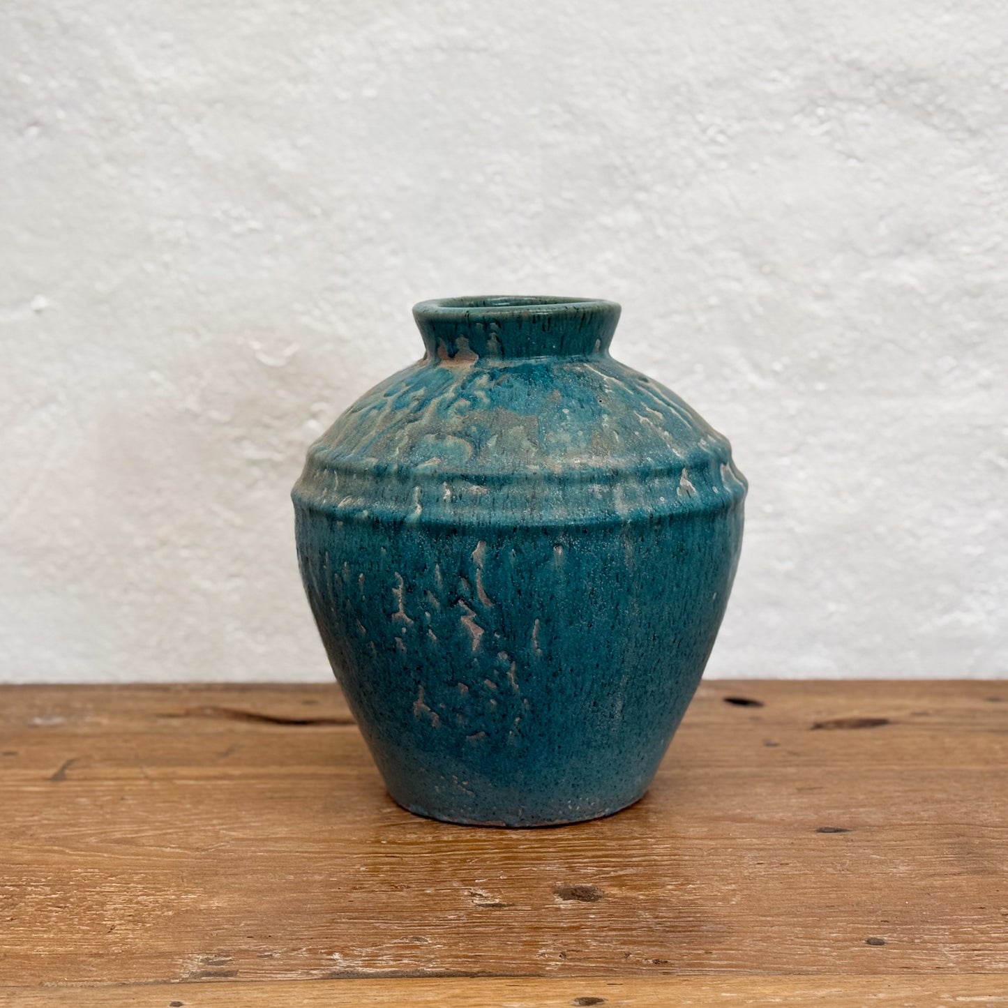 A blue mottled glaze ceramic pot placed on a wooden surface against a white background.
