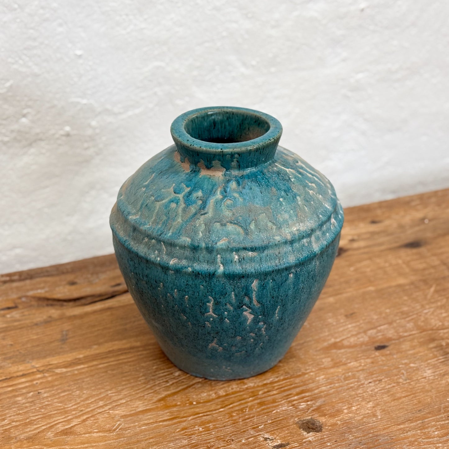 A blue mottled glaze ceramic pot placed on a wooden surface against a white background.