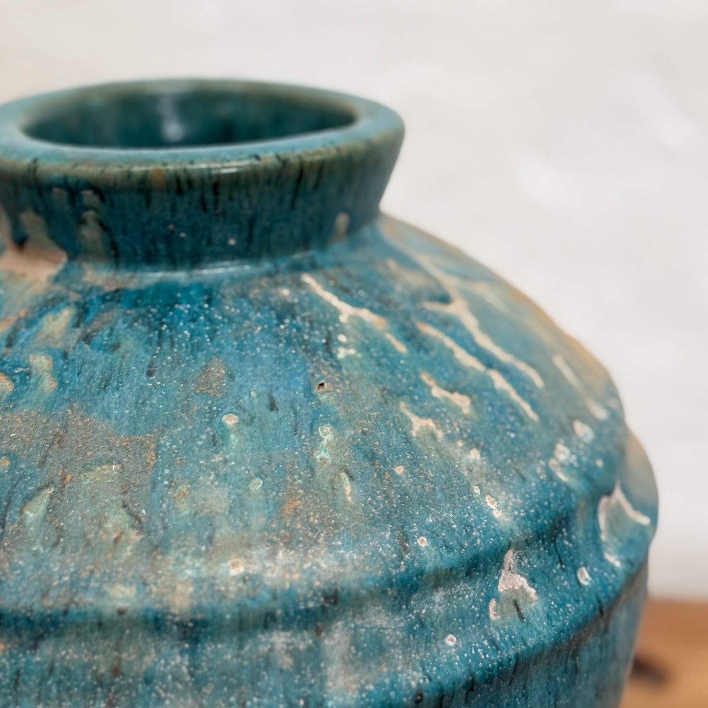 A blue mottled glaze ceramic pot placed on a wooden surface against a white background.