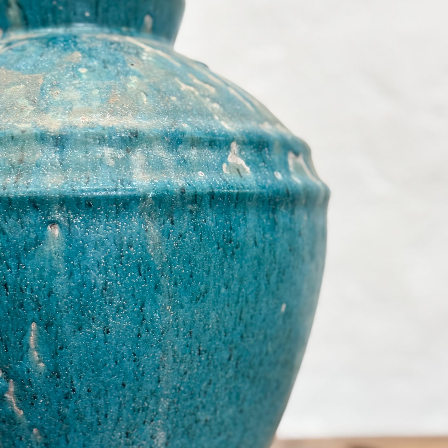 A blue mottled glaze ceramic pot placed on a wooden surface against a white background.