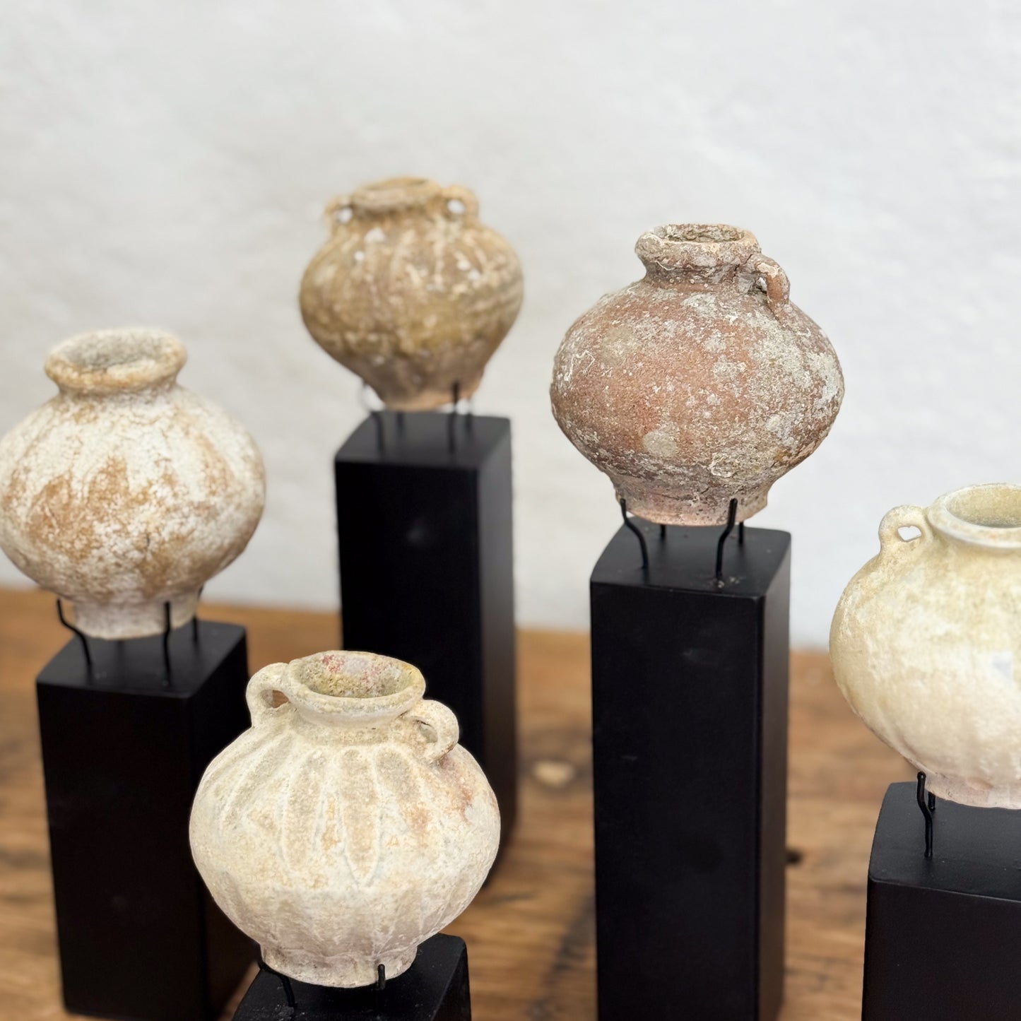 Set of ancient ceramic pots on black stands against a neutral background
