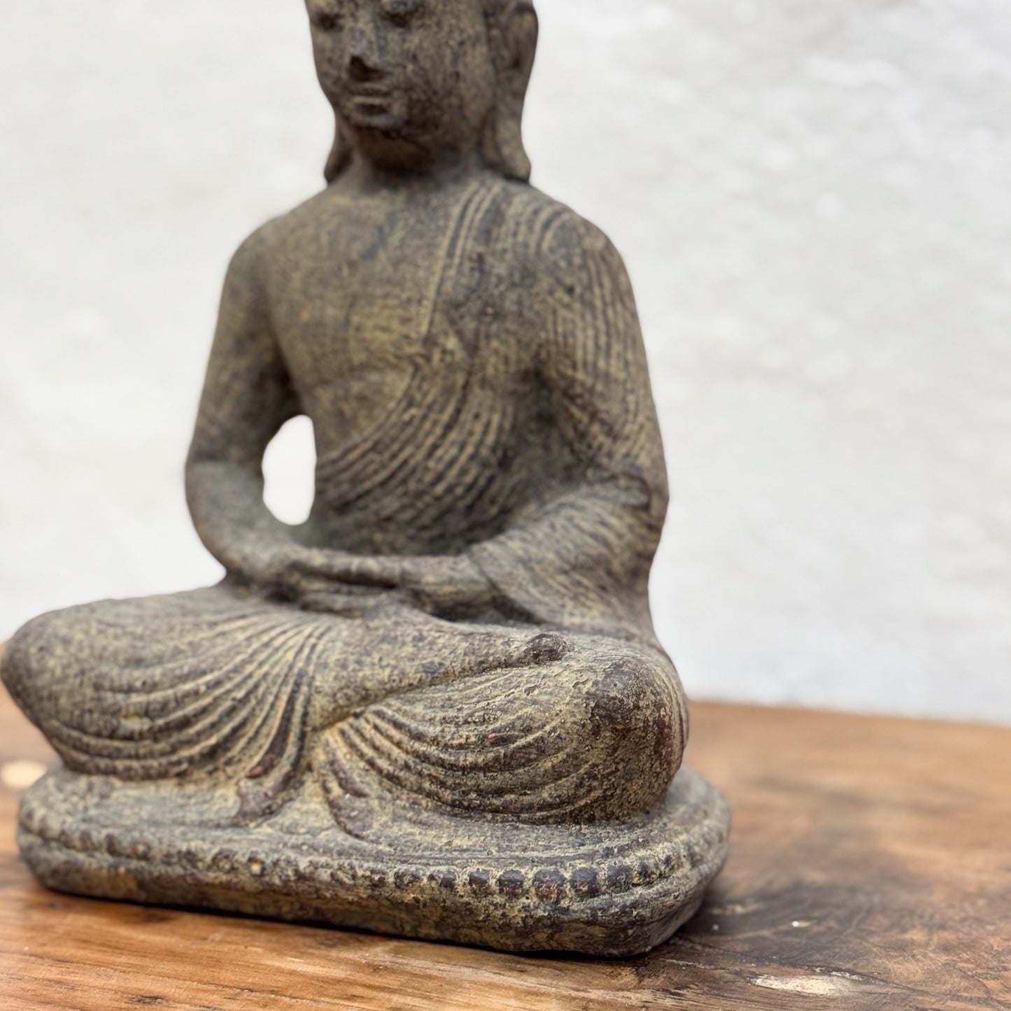 Stone statue of a meditating figure on a wooden surface with a white background