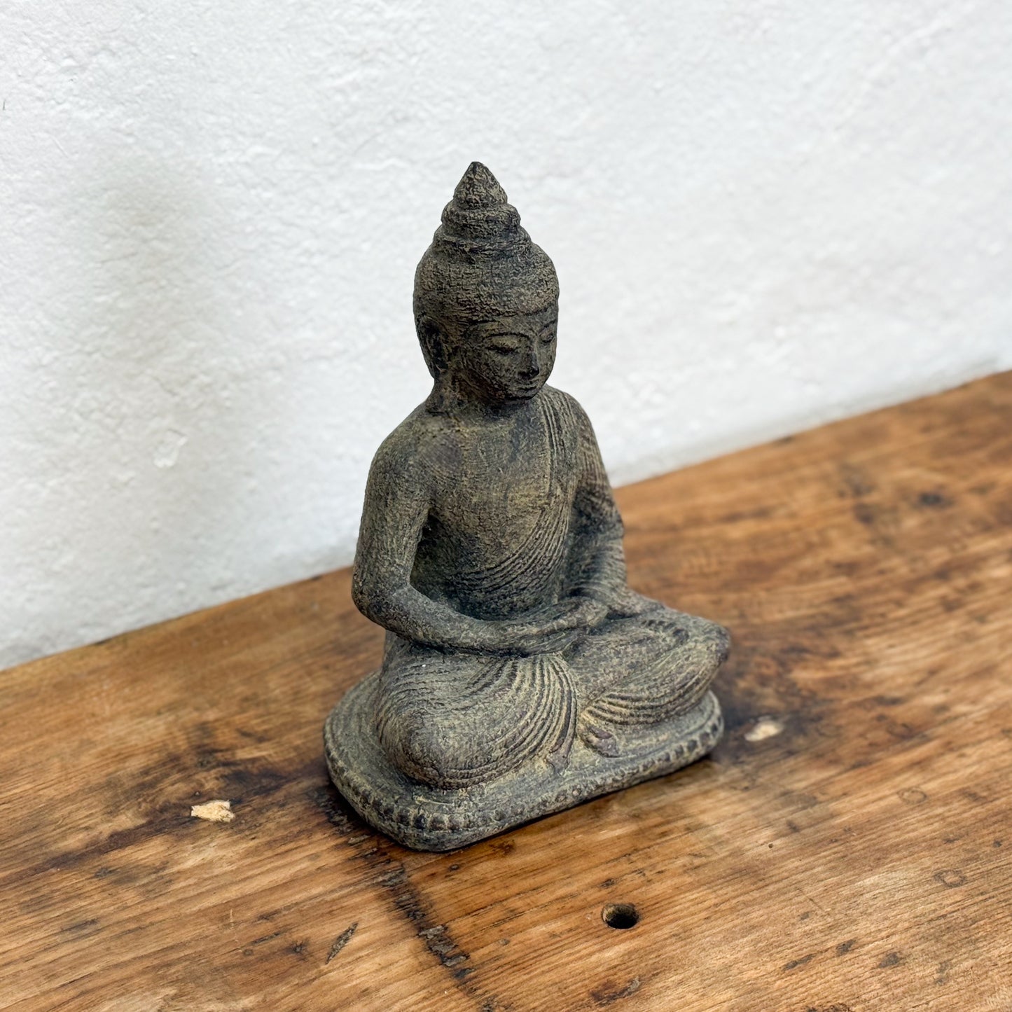 Stone Buddha statue on a wooden surface with a white textured wall background