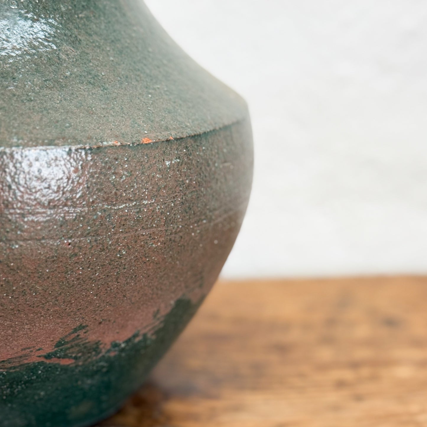 Close-up of a textured ceramic vase on a wooden surface with a blurred background