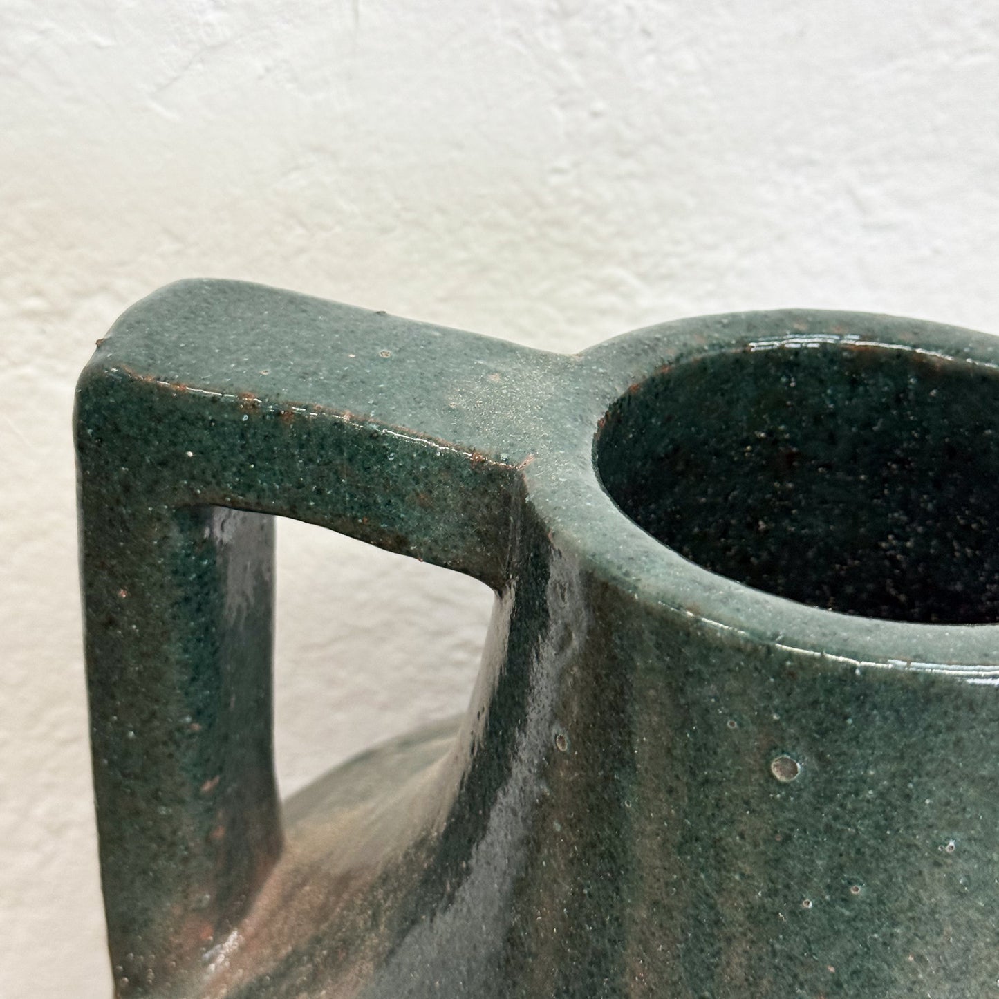 Close-up of a green ceramic mug handle and cup on a textured white background