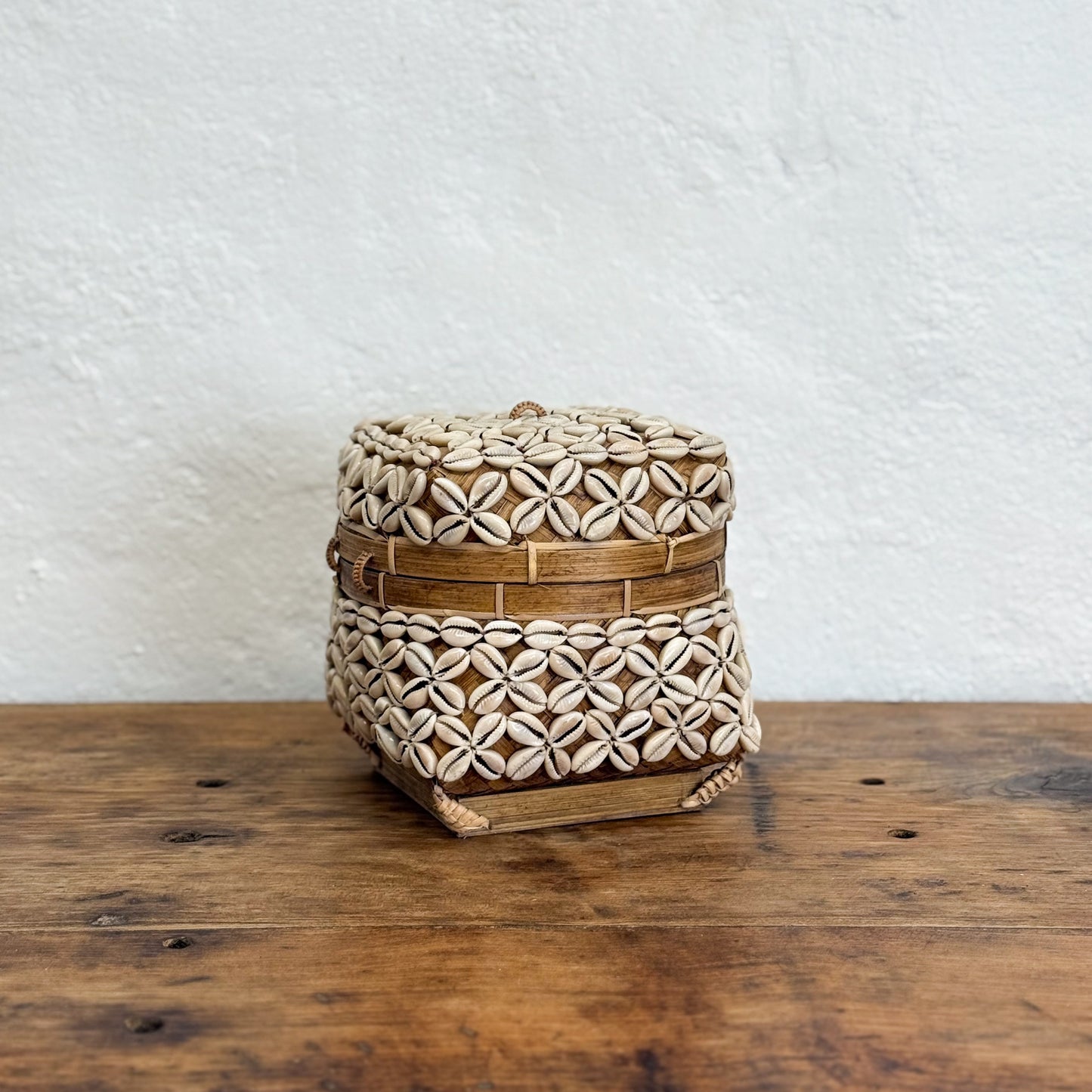 Woven basket with a lid on a wooden surface against a white wall