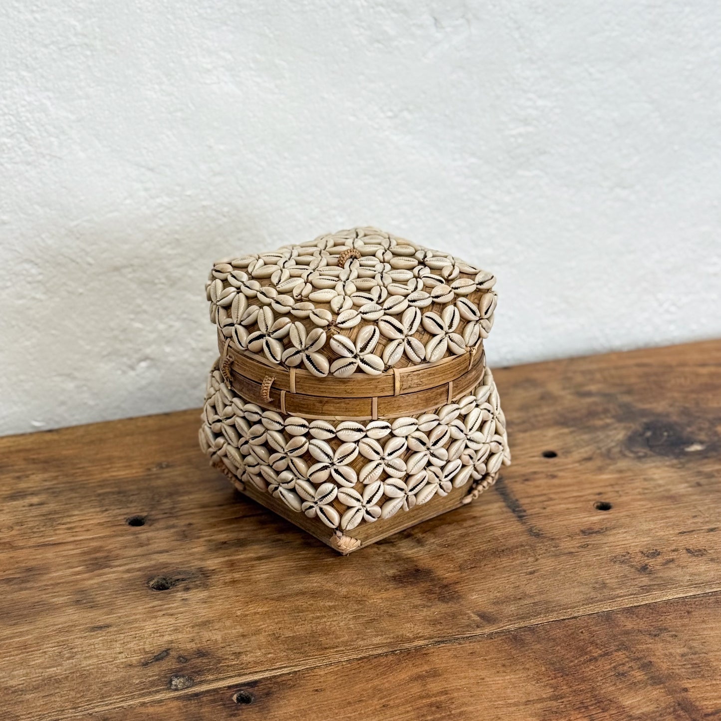 Woven hexagonal box on a wooden surface with a white textured wall background
