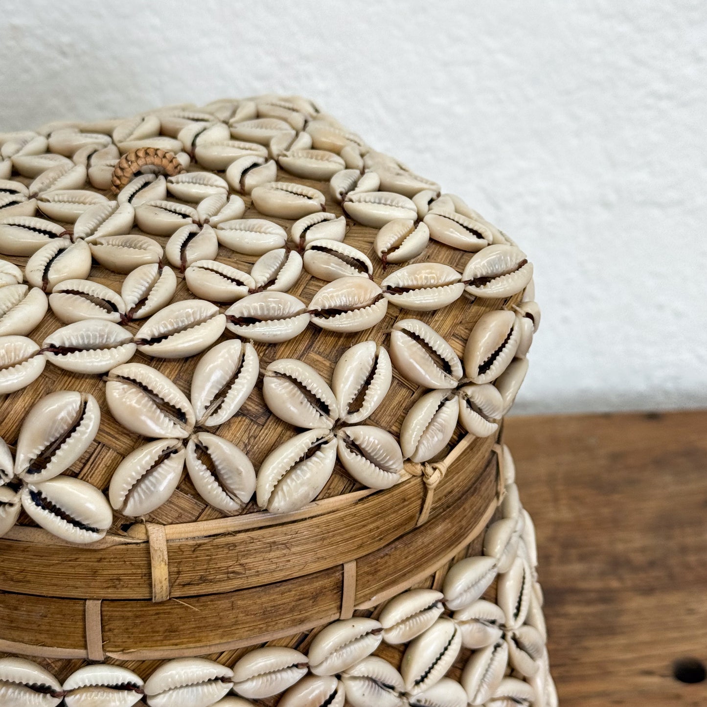 Decorative woven stool with cowrie shell pattern on a wooden floor.