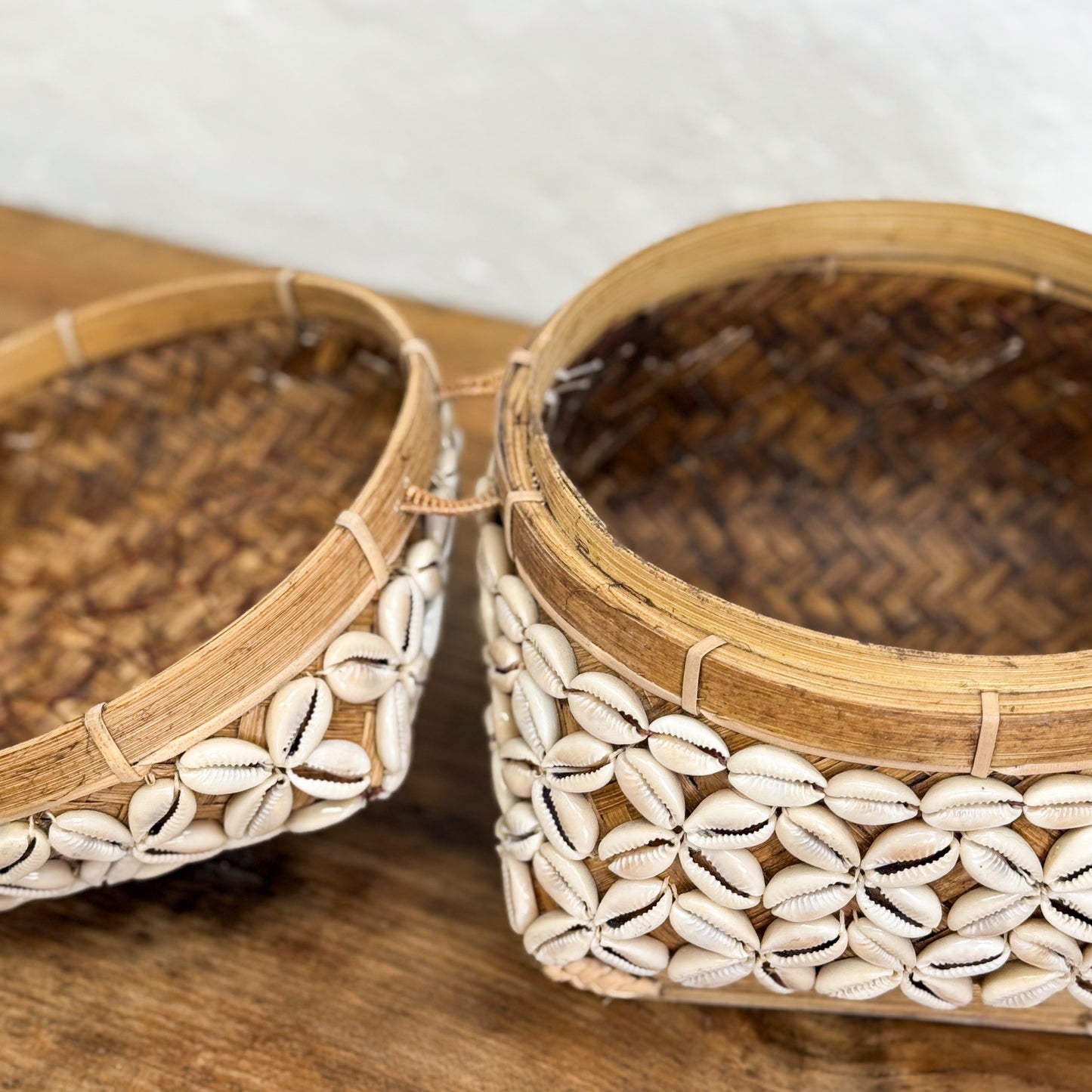 Two woven baskets with shell patterns on a wooden surface