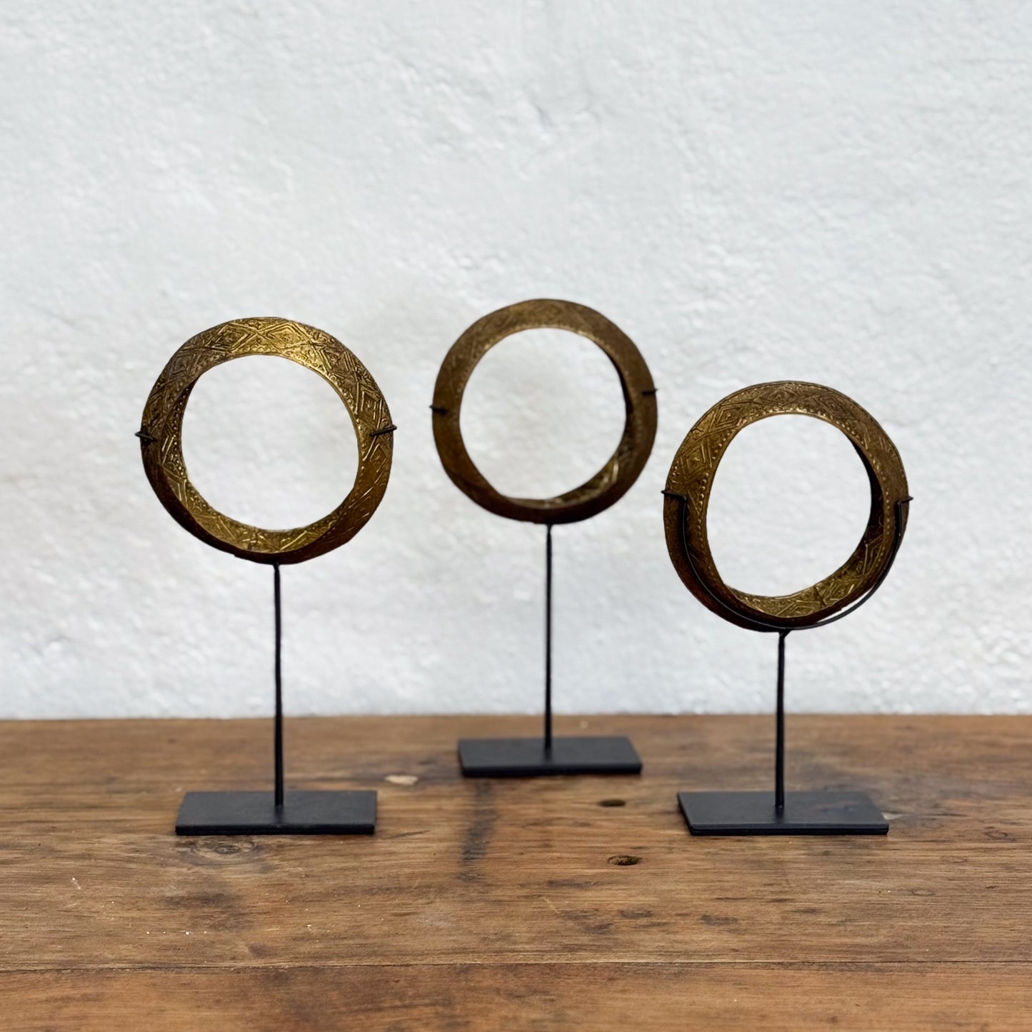 Three circular metal objects on stands against a textured white wall.