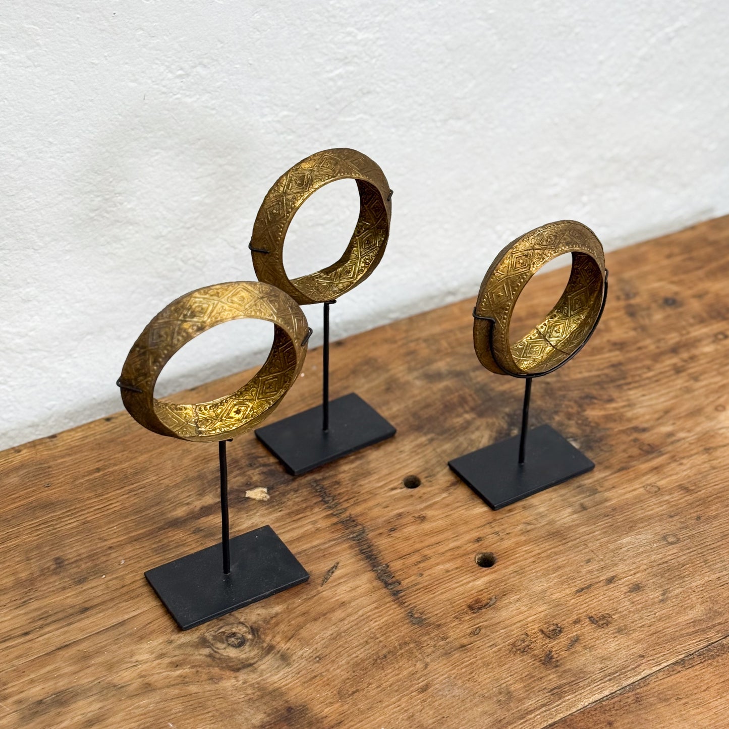 Three gold circular objects on black stands against a textured white wall.