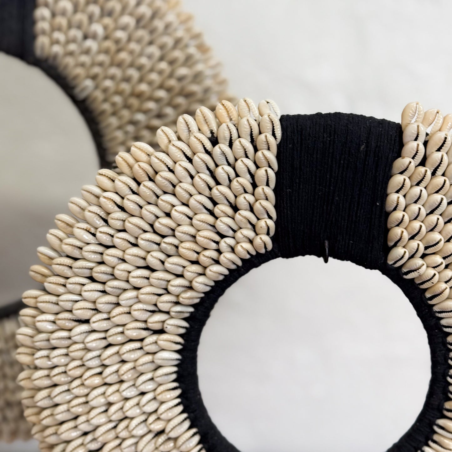 Decorative wreath with black and beige shell-like material on a neutral background
