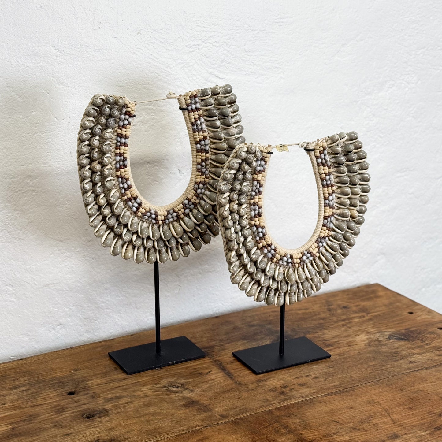 Pair of beaded necklaces on stands against a white wall
