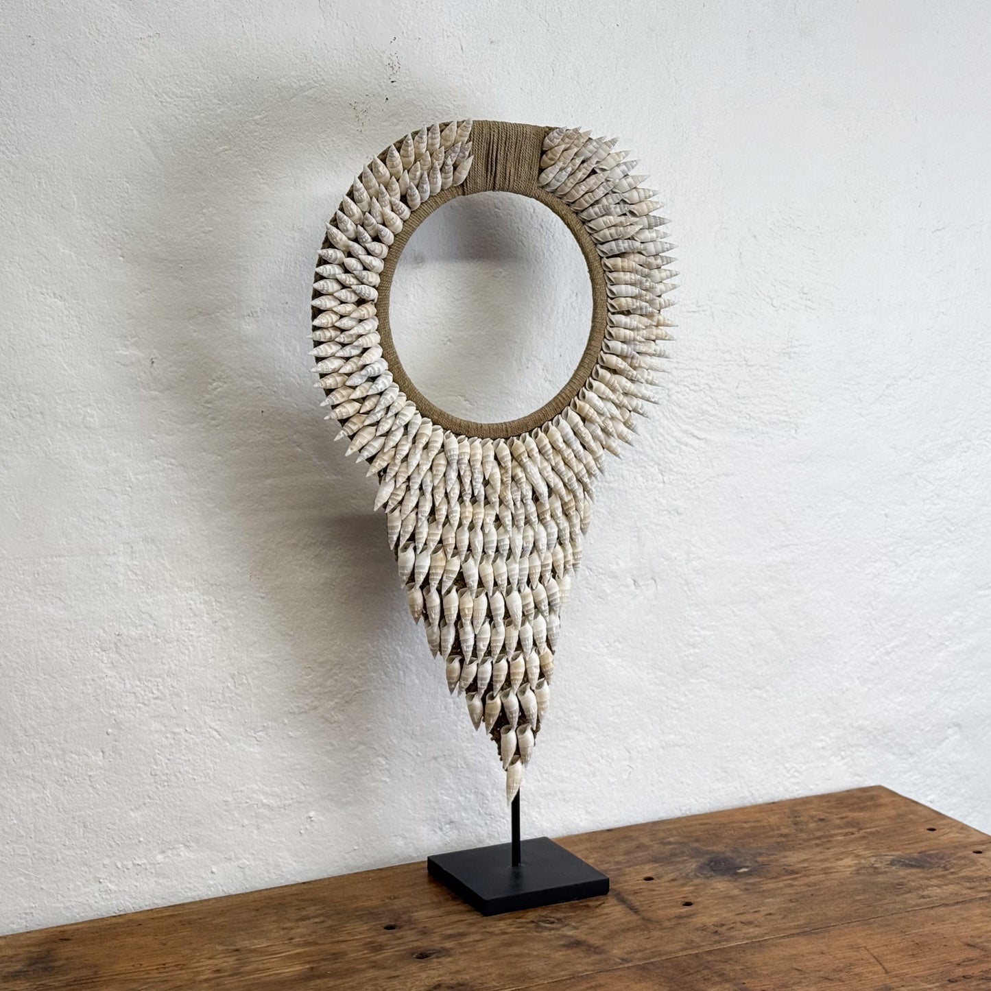 Decorative shell mirror on a wooden stand against a white wall