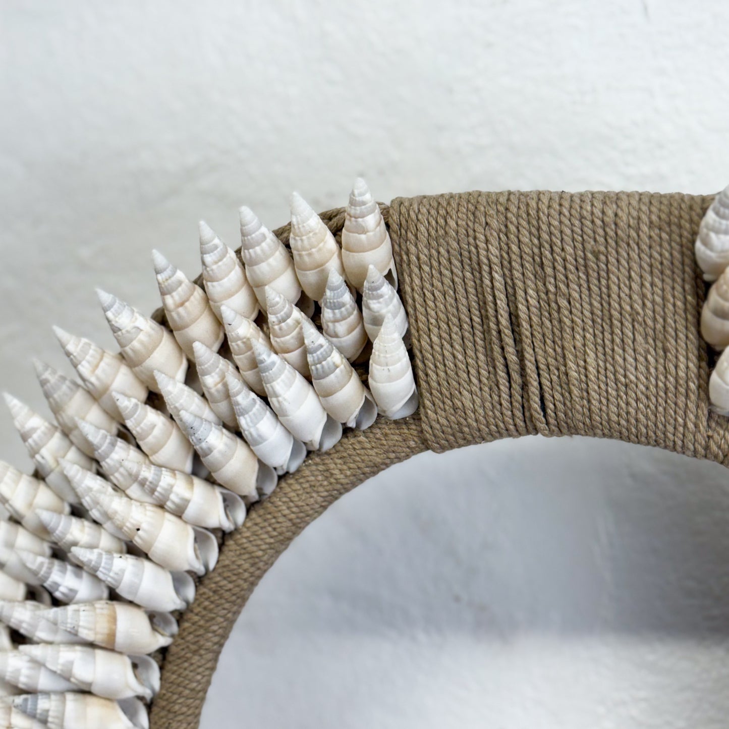 Decorative wreath made of white shells and brown rope on a white background
