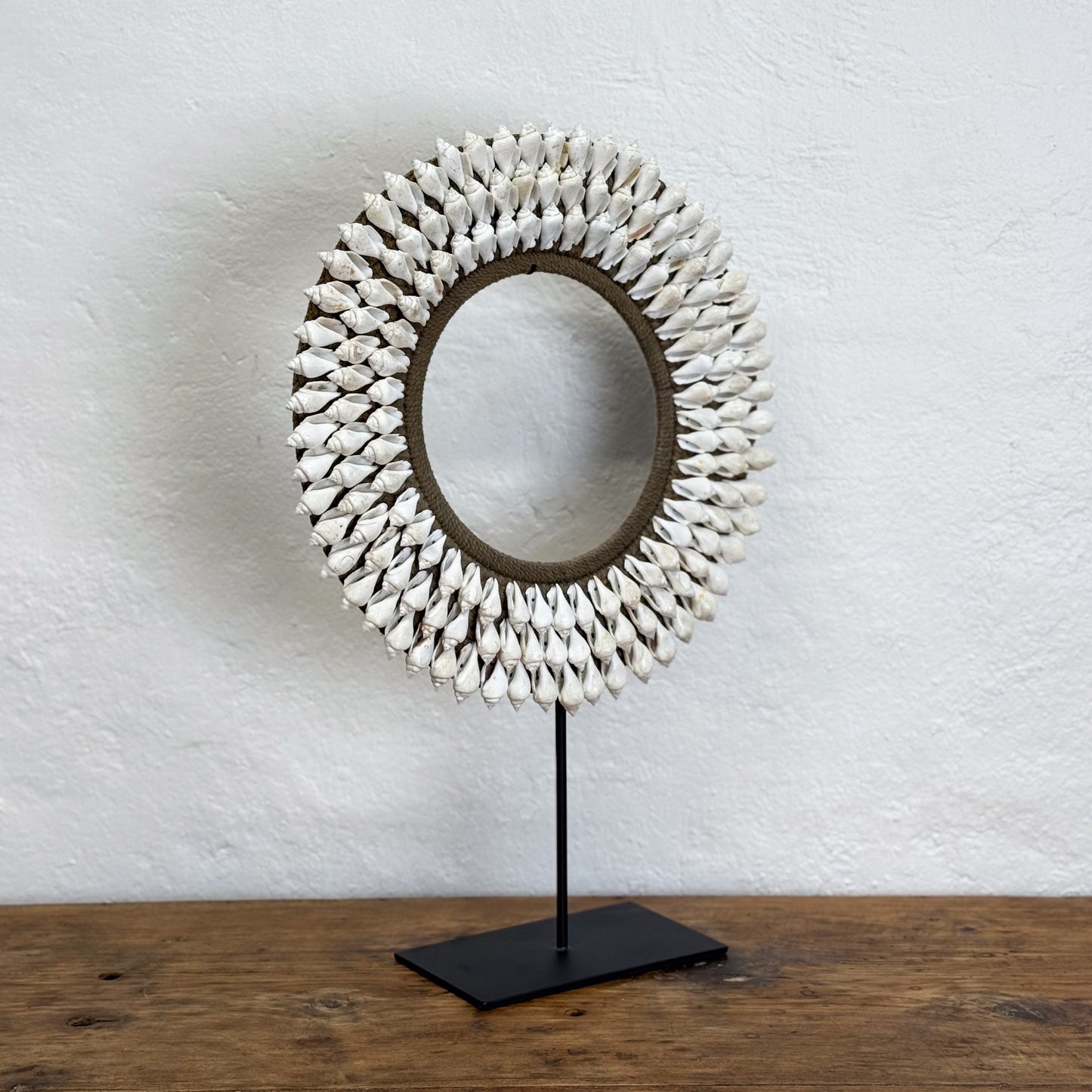 Decorative mirror with shell-like design on a stand against a white wall.