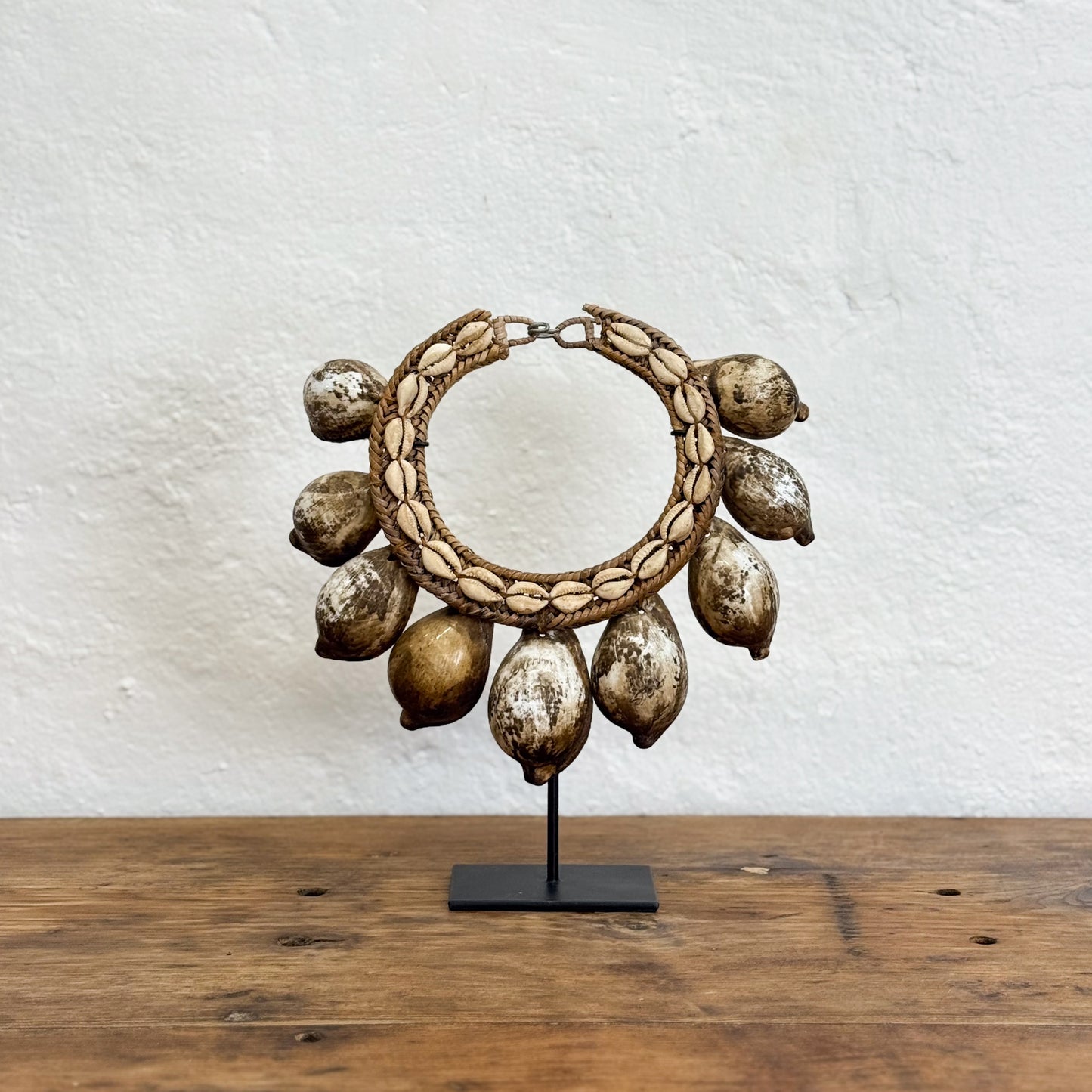Decorative hoop with shell-like elements on a stand against a textured white wall.