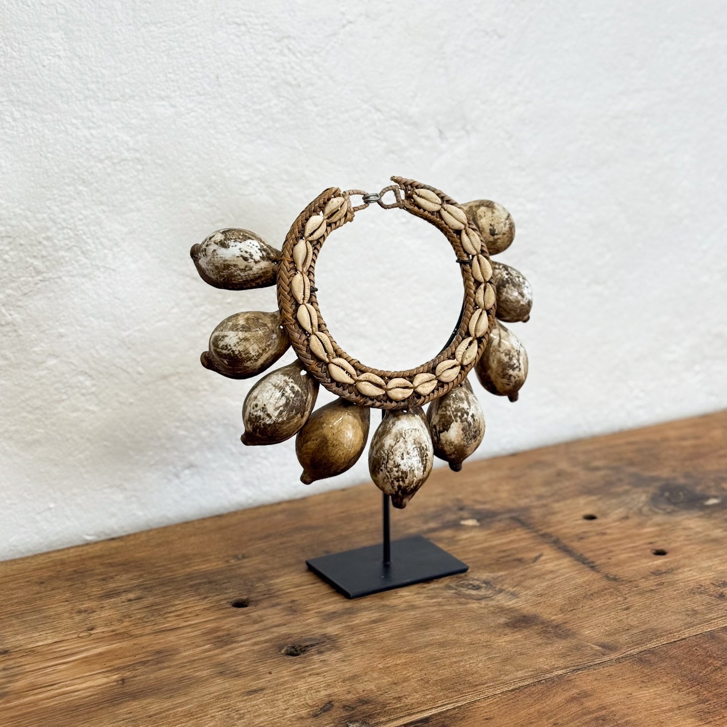 Decorative hoop earring with natural elements on a stand against a white wall.