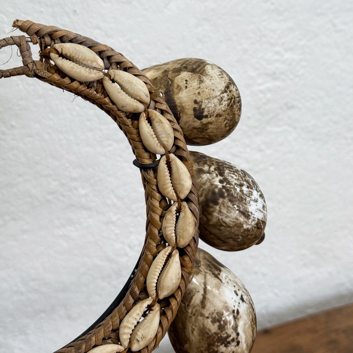 Decorative item with cowrie shells and woven material on a textured white background