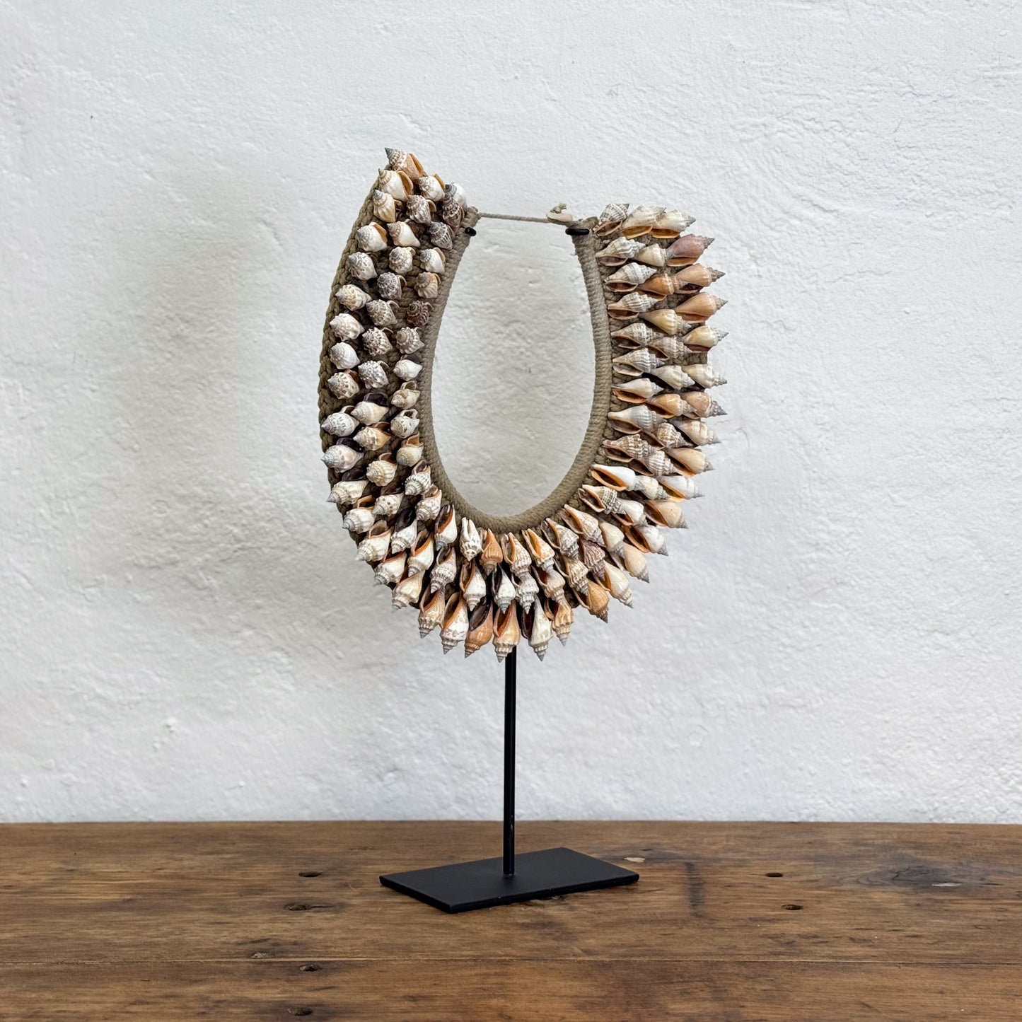Shell necklace on a stand against a textured white wall