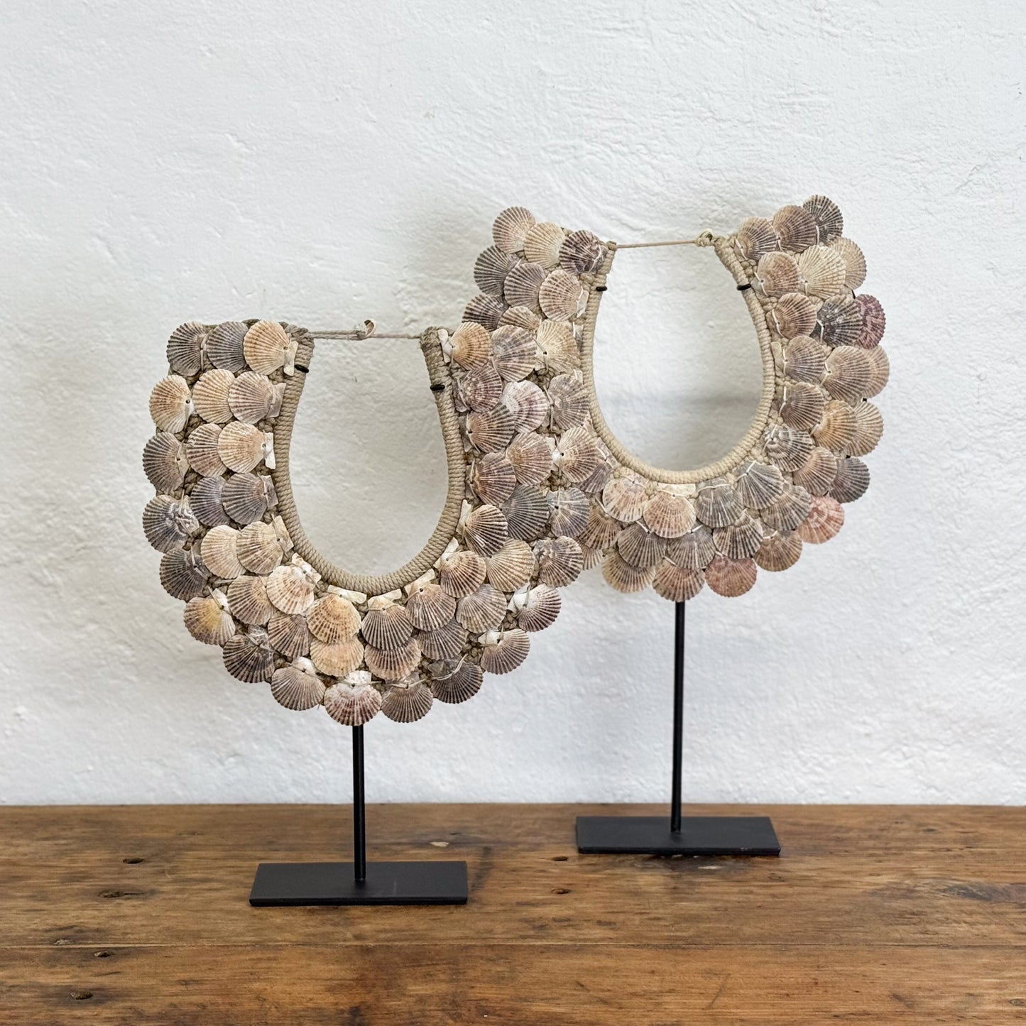 Two shell-encrusted mirrors on stands against a textured white wall.
