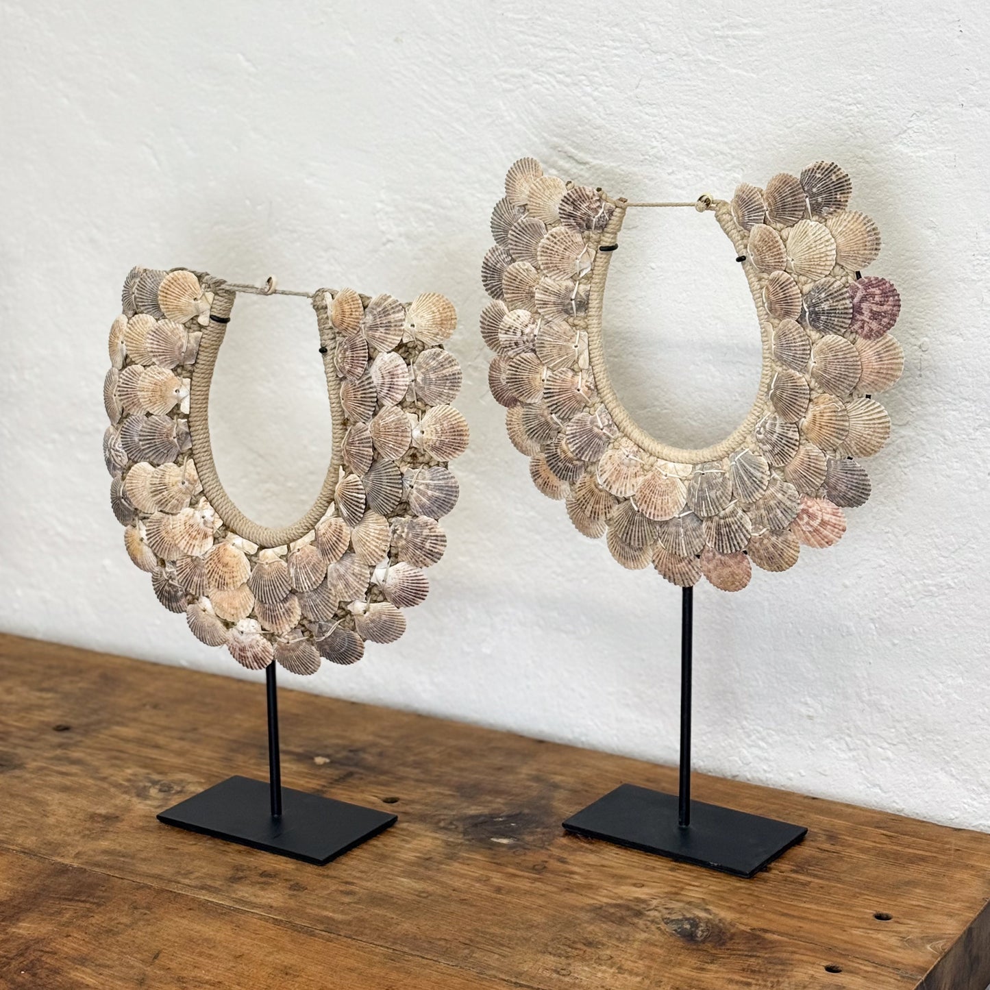 Two shell necklaces on stands against a white wall.