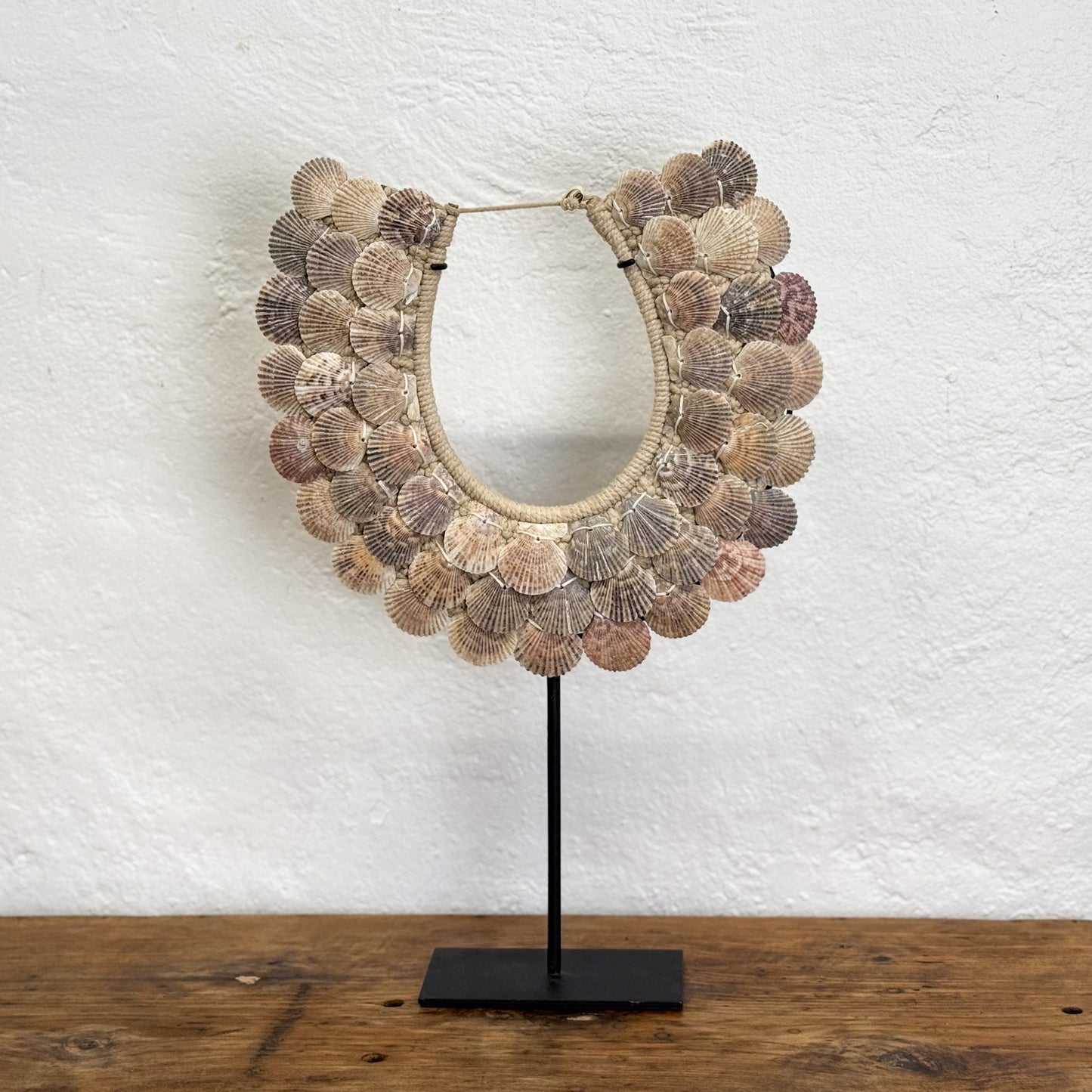 Decorative mirror with shell-like design on a stand against a white textured wall.