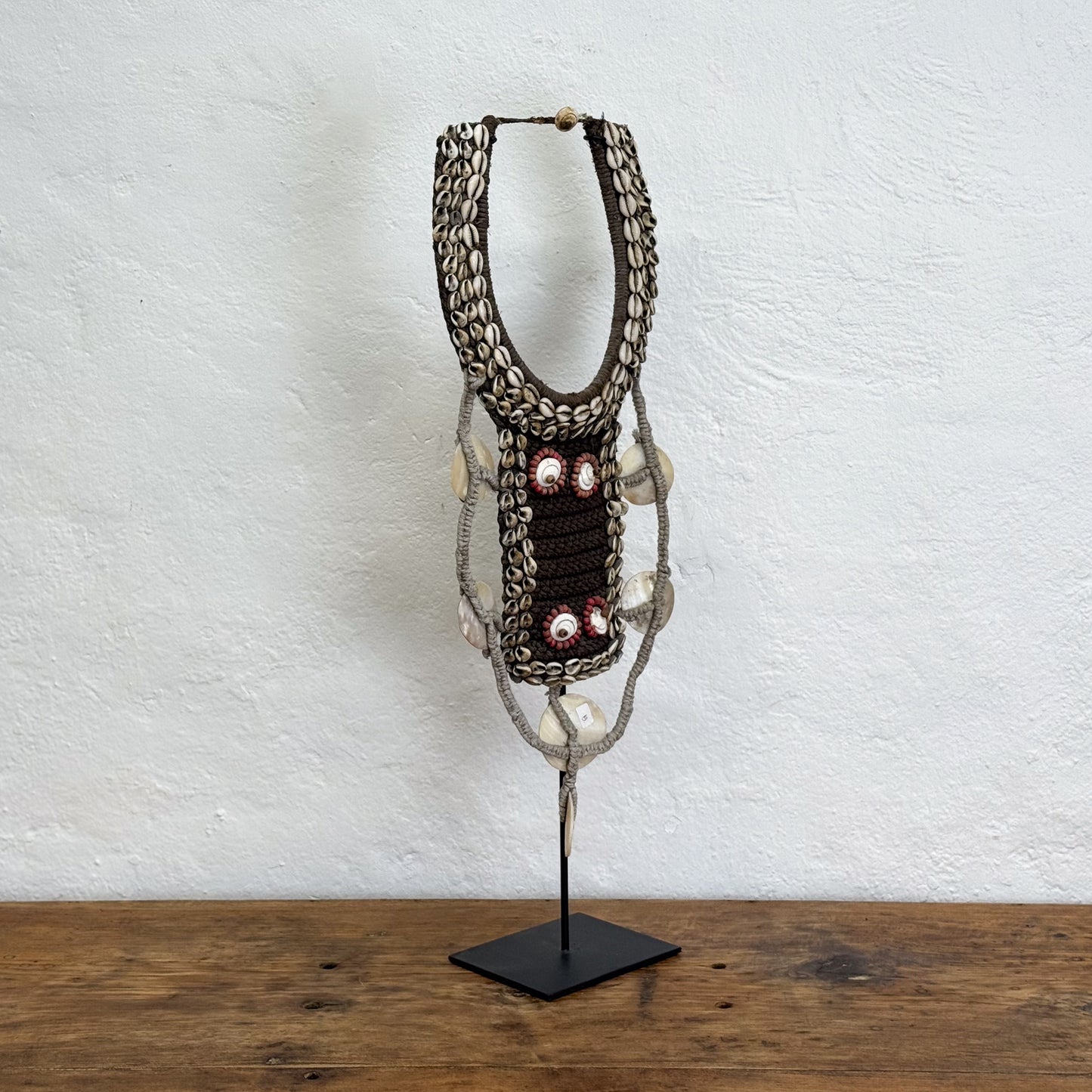 Decorative macramé wall hanging on a stand against a white wall.