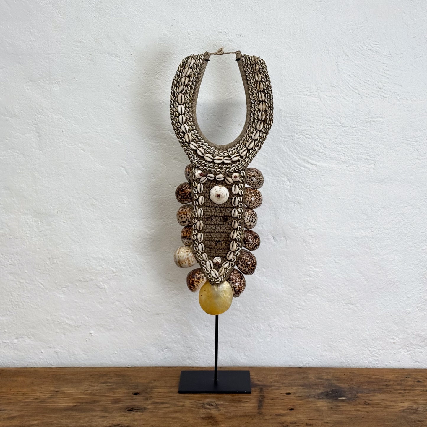 Decorative necklace on a stand against a textured white wall