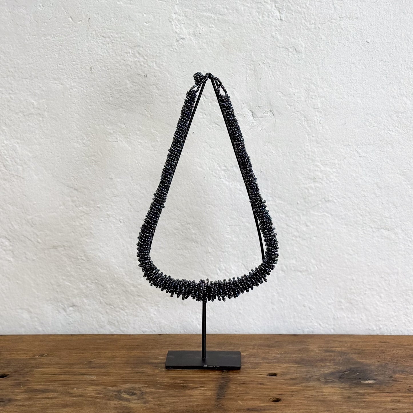 Black beaded necklace on a stand against a white wall