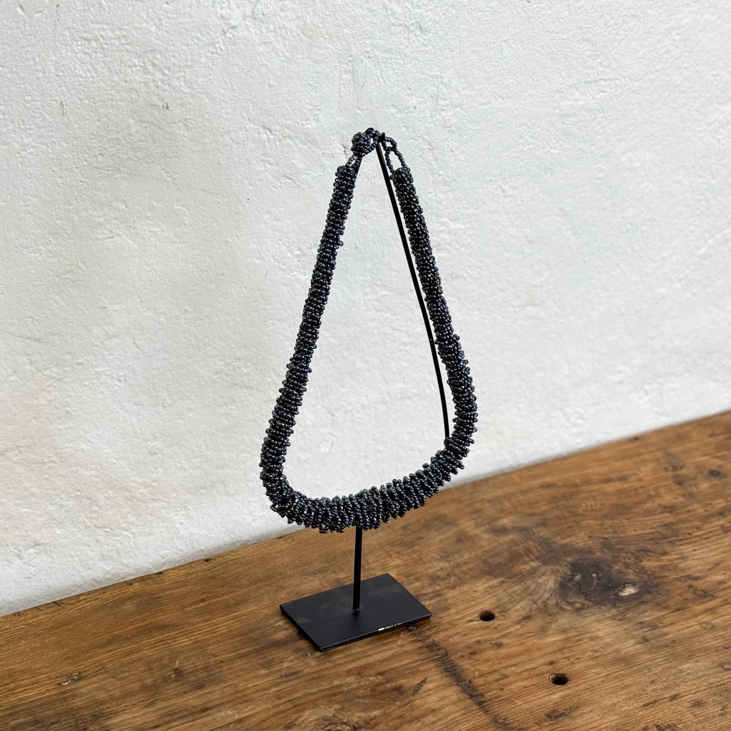 Black beaded necklace on a stand against a white wall