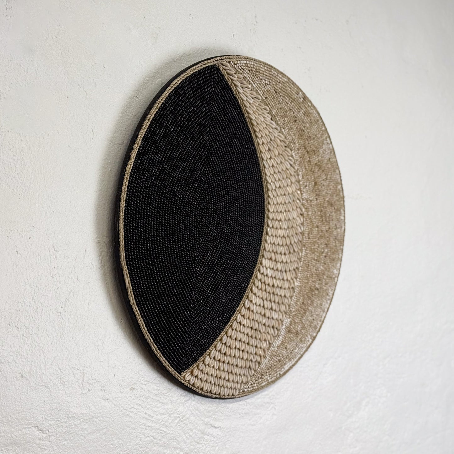 Round woven mat with black center and beige edges on a light gray background