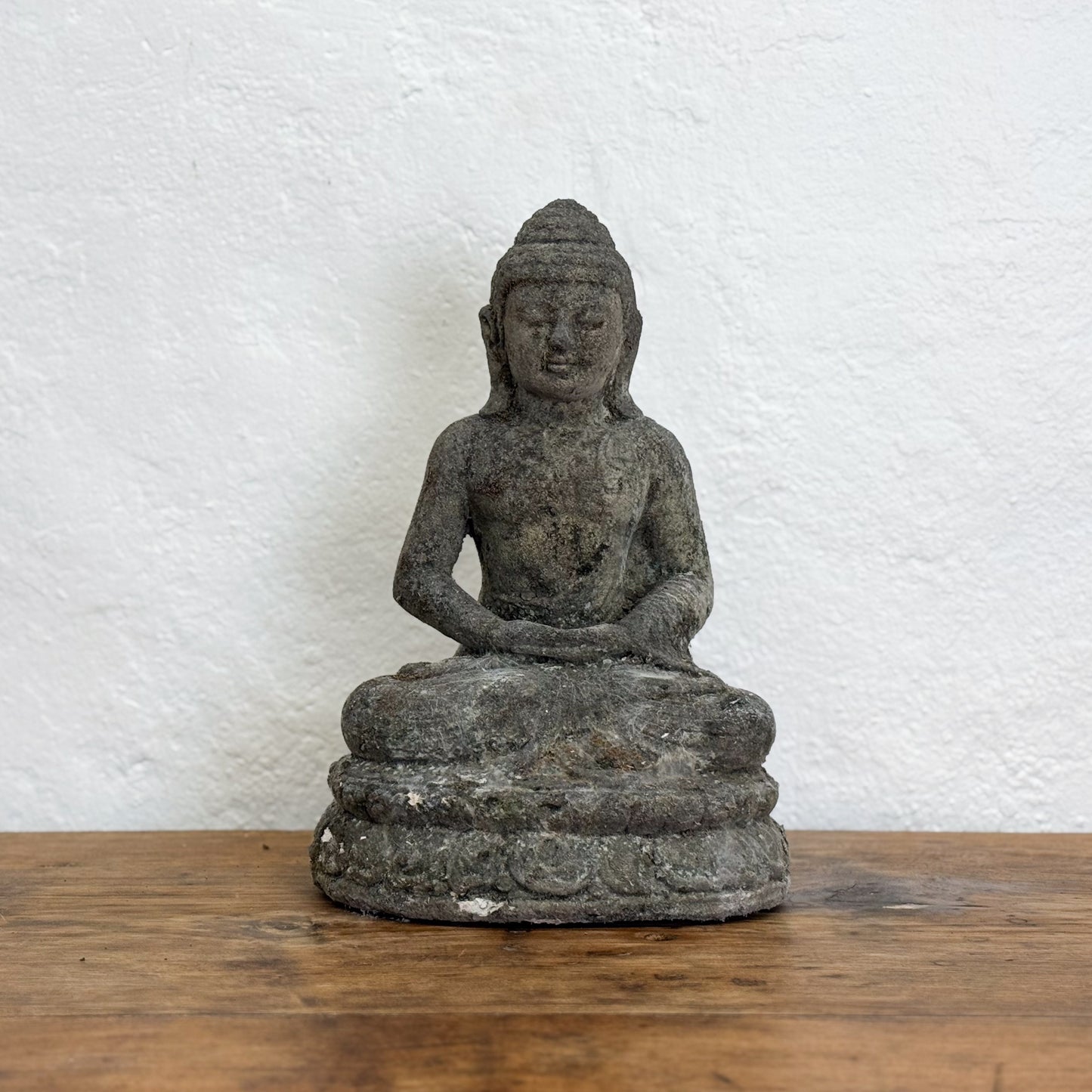 Stone Buddha statue on a wooden surface with a white textured wall background