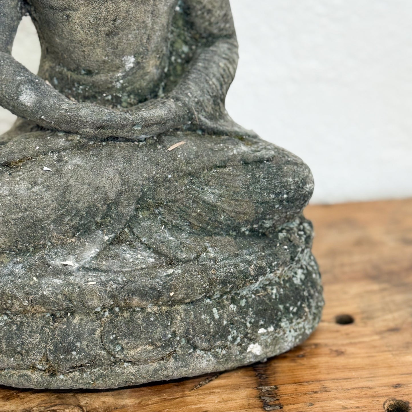 Stone statue of a seated figure on a wooden surface with a white background