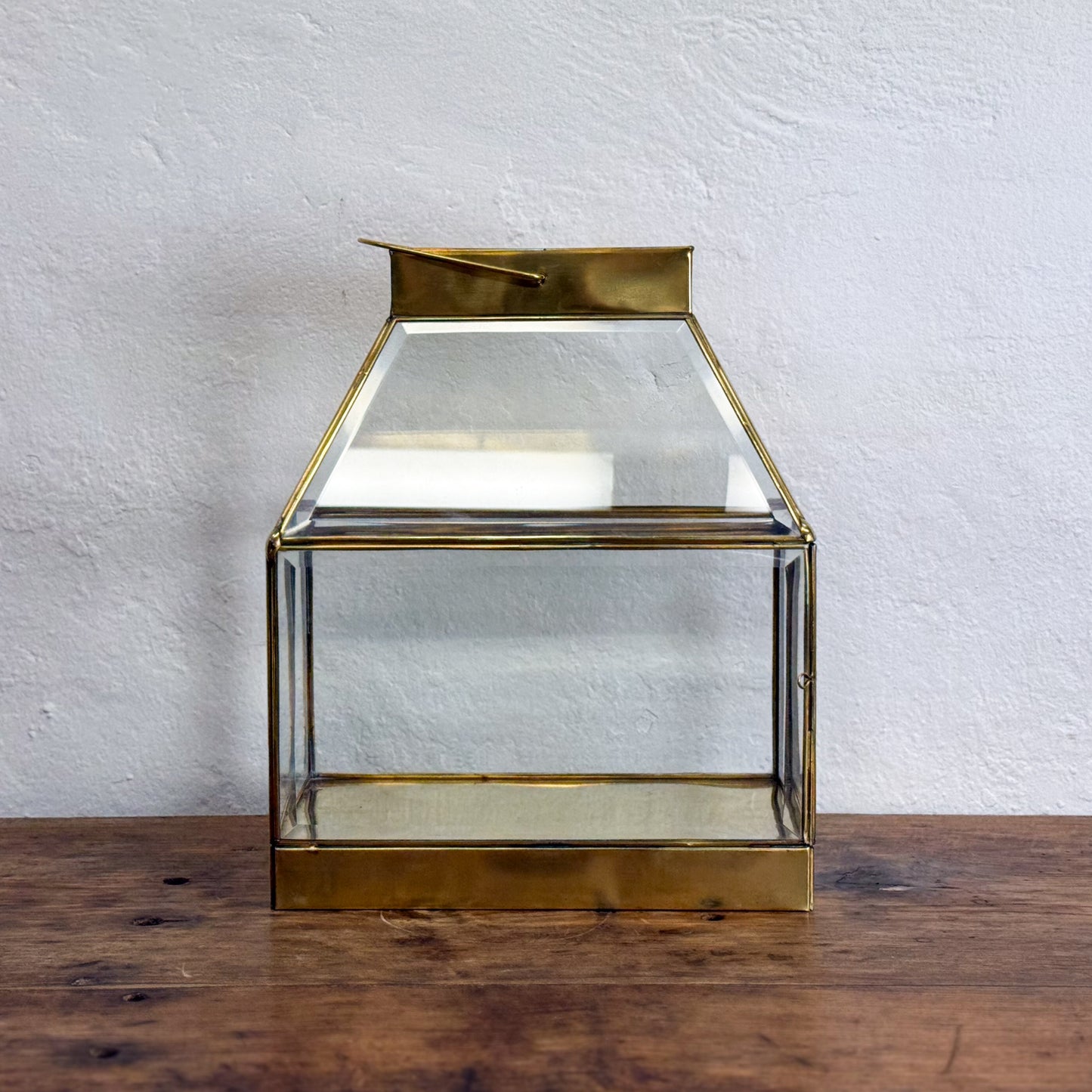 Gold and glass lantern on a wooden surface with a white textured wall background