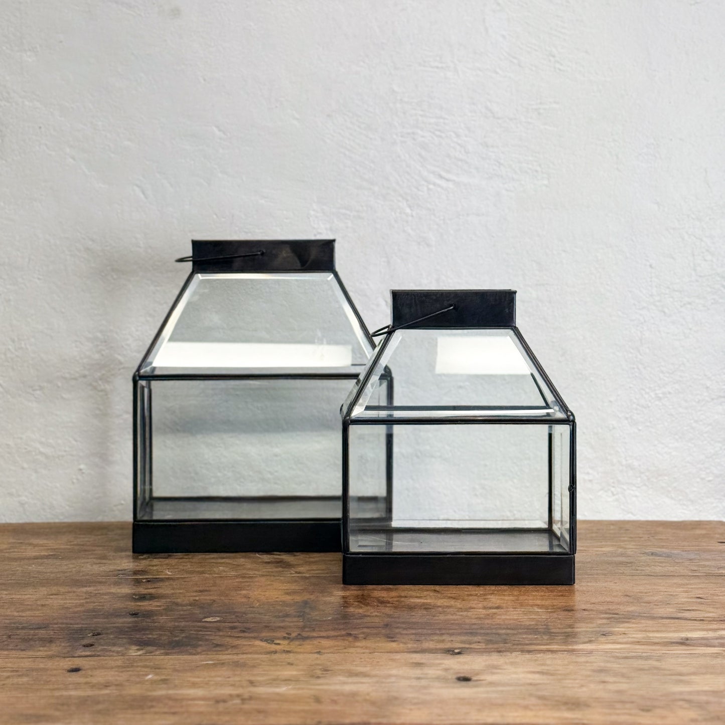 Two glass display cases with black metal frames on a wooden surface.